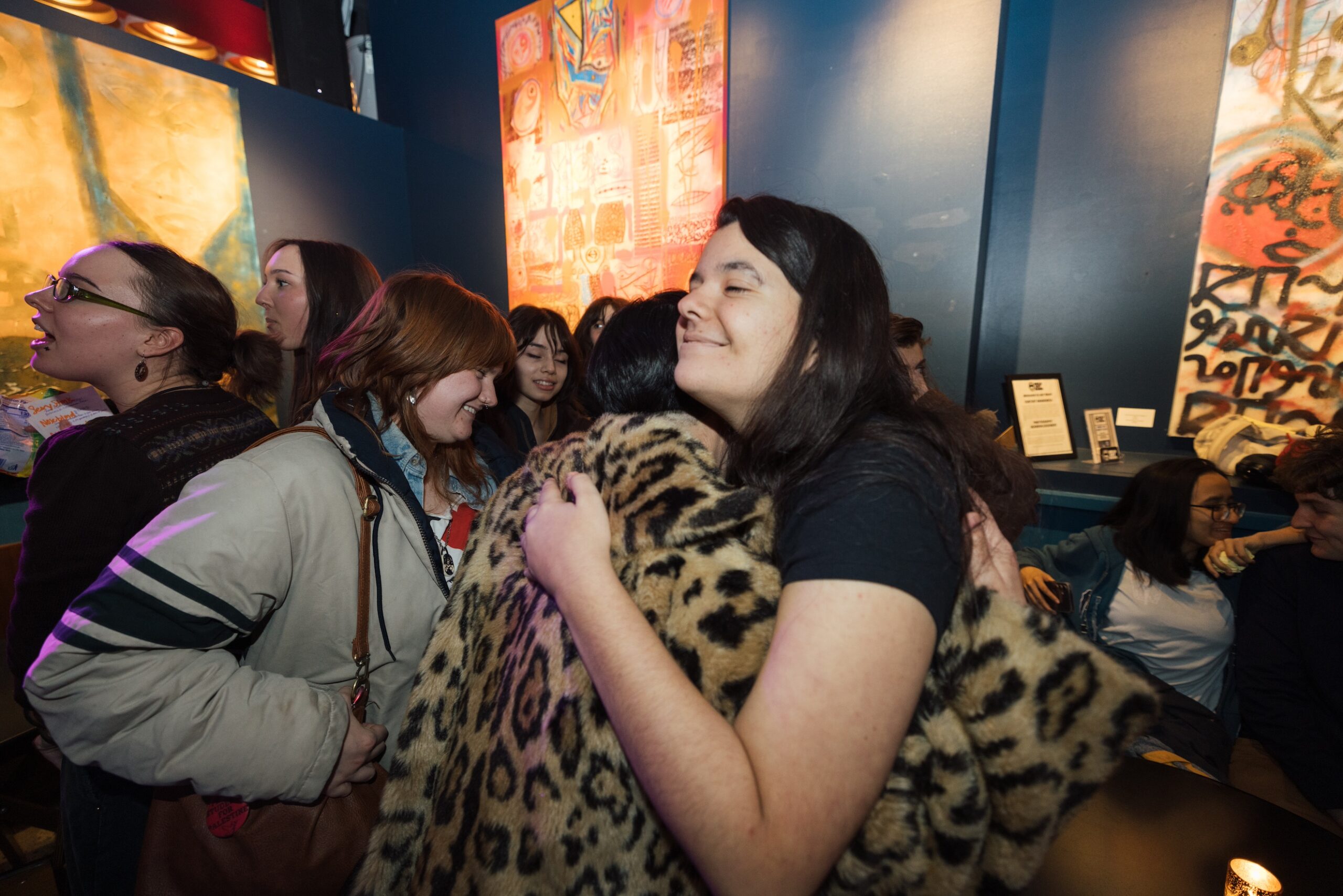 Wide-angle shot of a performer hugging an audience member in a crowd of people in the venue