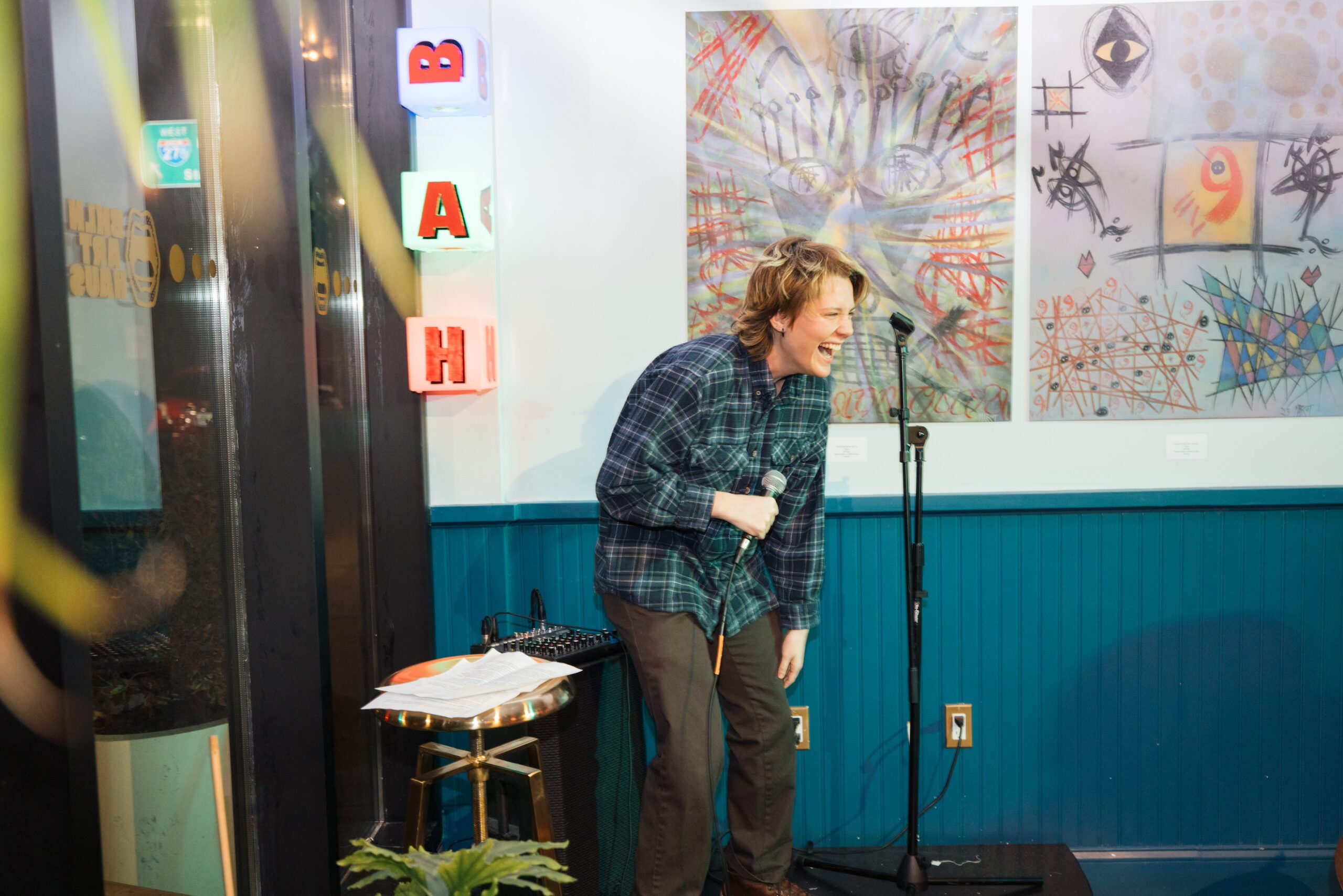 A student performer on stage during their stand-up comedy act, facing the audience and doubled-over laughing