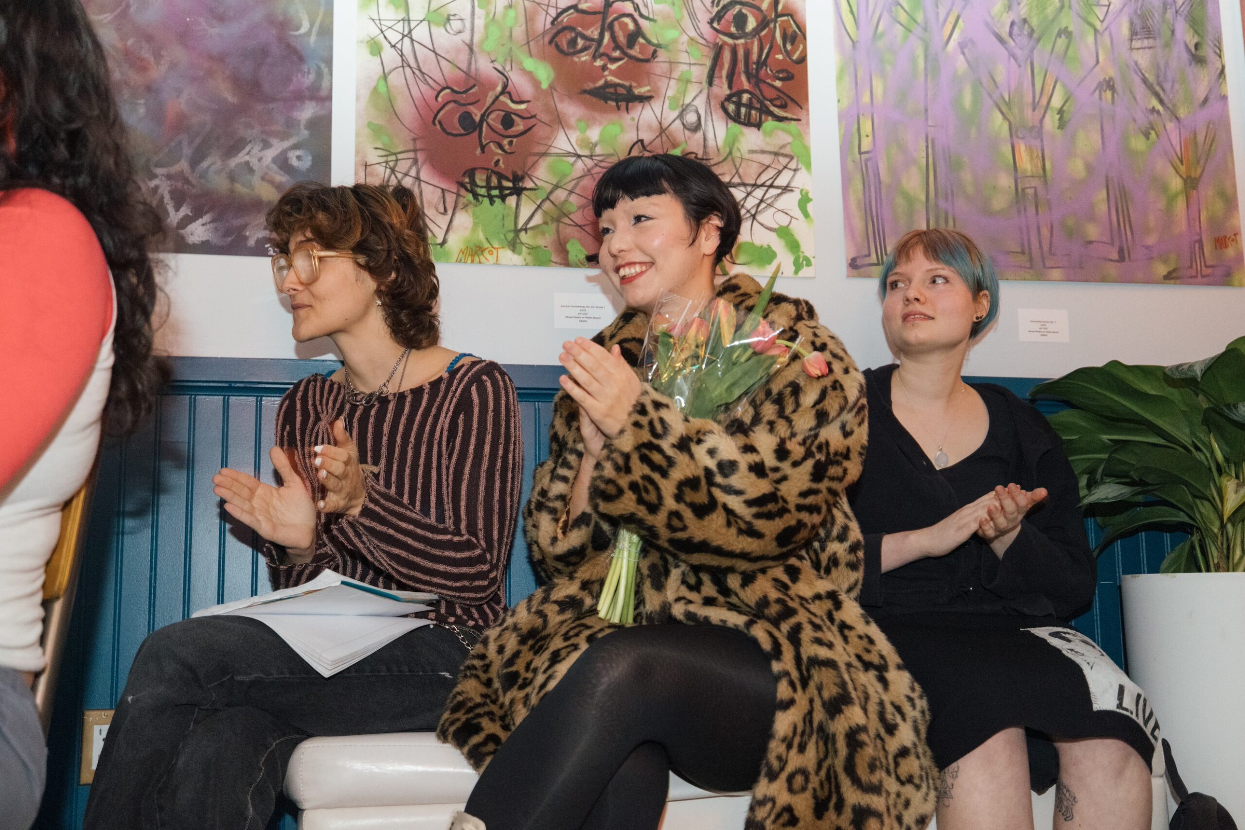 Three student performers sit on a bench, smiling and applauding