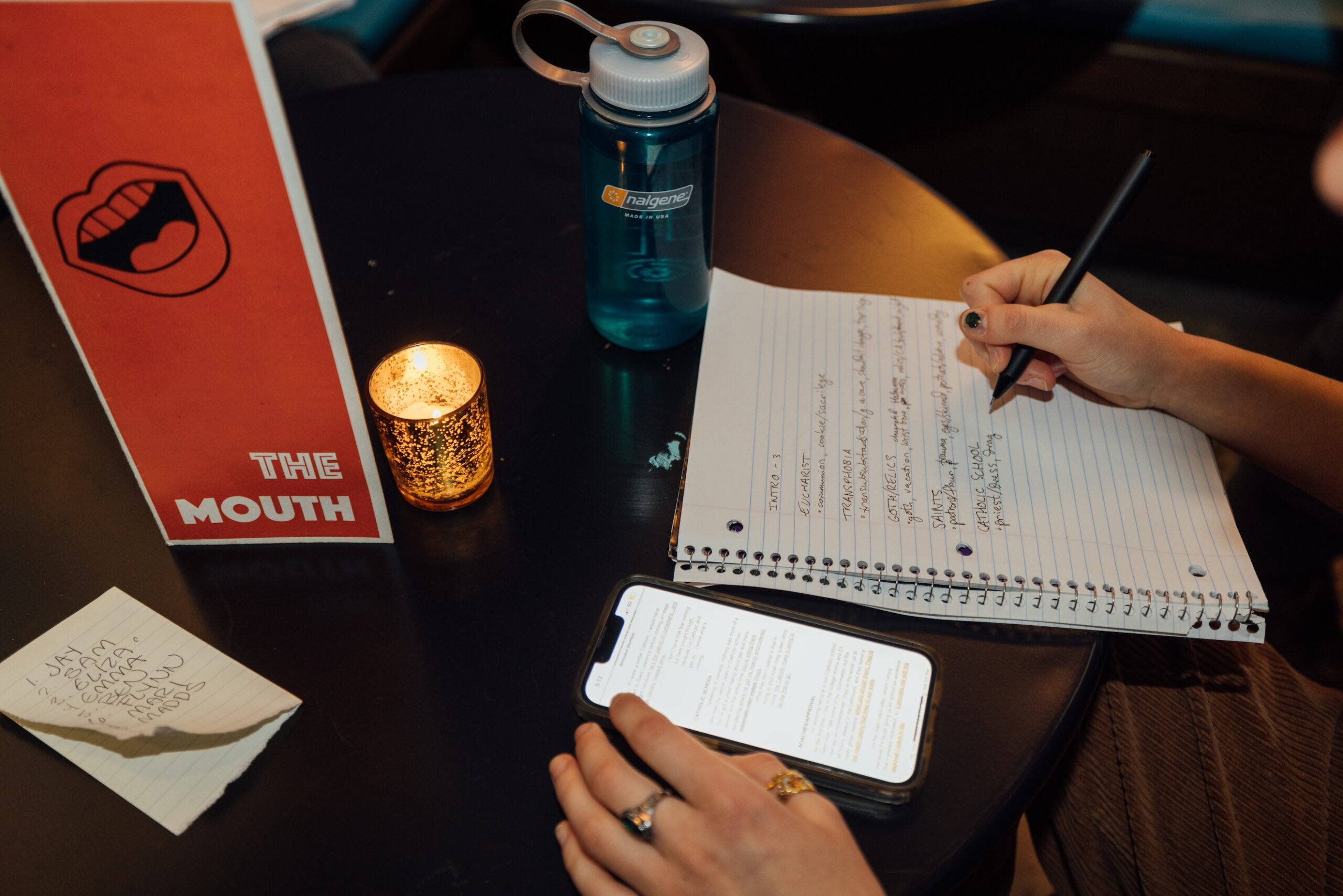 Close-up of someone transcribing performance notes from their phone onto a piece of notebook paper at a table