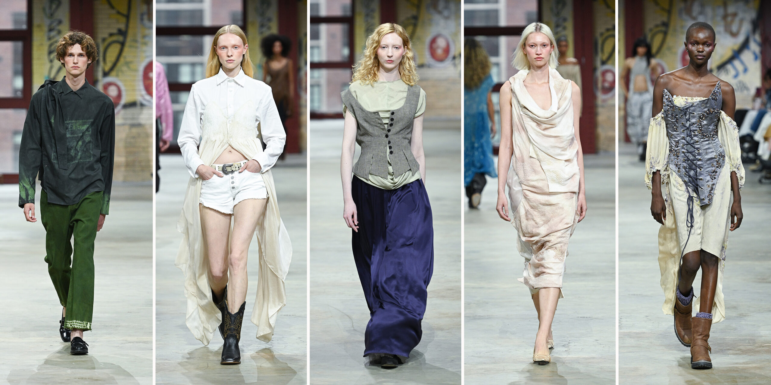 A composite image showing five models walking a fashion runway against a backdrop of graffiti-covered brick walls and tall windows. From left to right: The first model wears a dark green button-up top with a distressed texture and olive green pants, paired with black shoes. The second model wears a white collared shirt with textured details, white cut-off shorts, and sheer cream fabric panels trailing from the waist. They complete the look with black cowboy boots and a silver belt. The third model wears a ruched light green top under a gray pinstripe corset vest, paired with a flowing deep purple satin skirt. The fourth model wears a draped, cream-toned dress with an asymmetrical silhouette and a layered, cowl-neck design in soft, textured fabrics. The fifth model wears a striking off-the-shoulder corset dress with a lavender bodice and cream sleeves and skirt, adorned with floral embroidery and lace-up details. The look is paired with brown ankle boots and lilac socks.