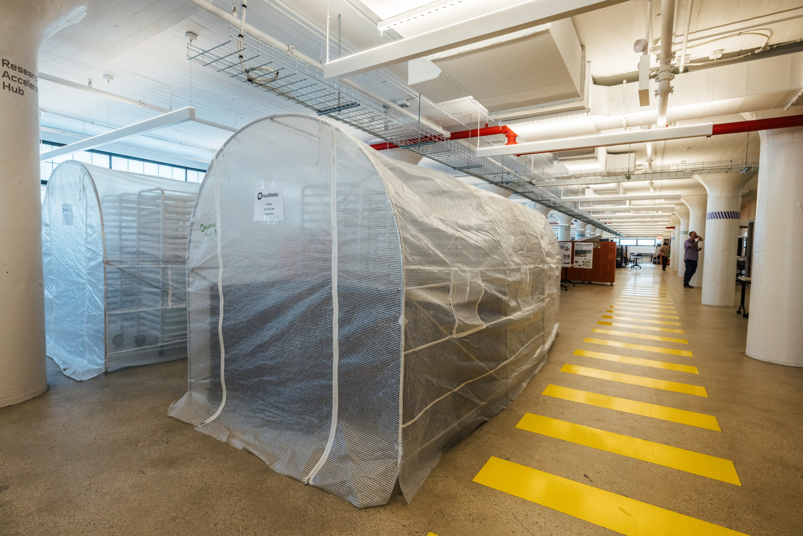 Indoor lab or research space featuring two transparent mesh greenhouses labeled