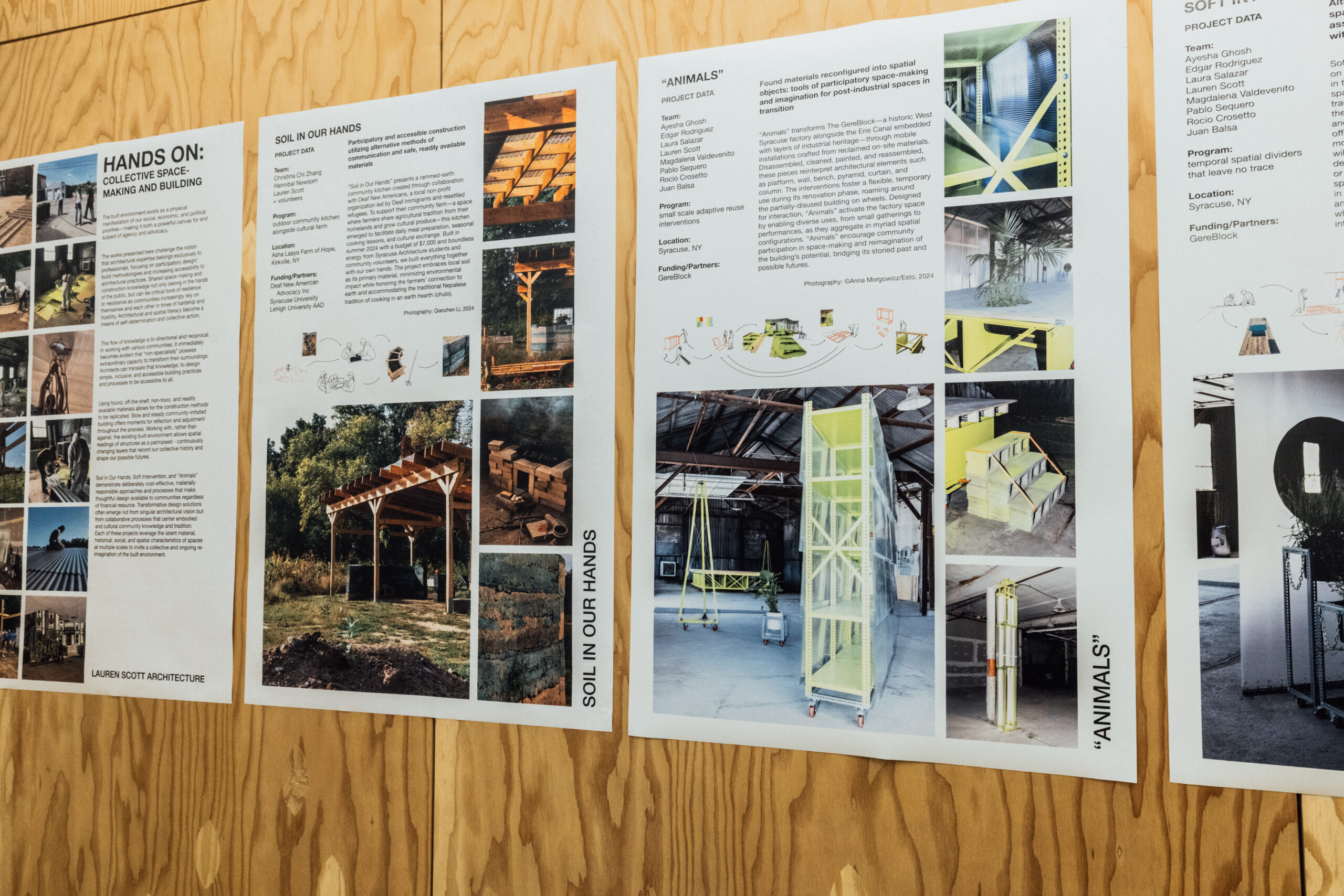 Photo of an exhibition wall displaying four vertically oriented architecture project posters mounted on a wooden surface. Each poster features a different student or group design under the theme “Hands On: Collective Space-Making and Building.” The posters include project titles such as