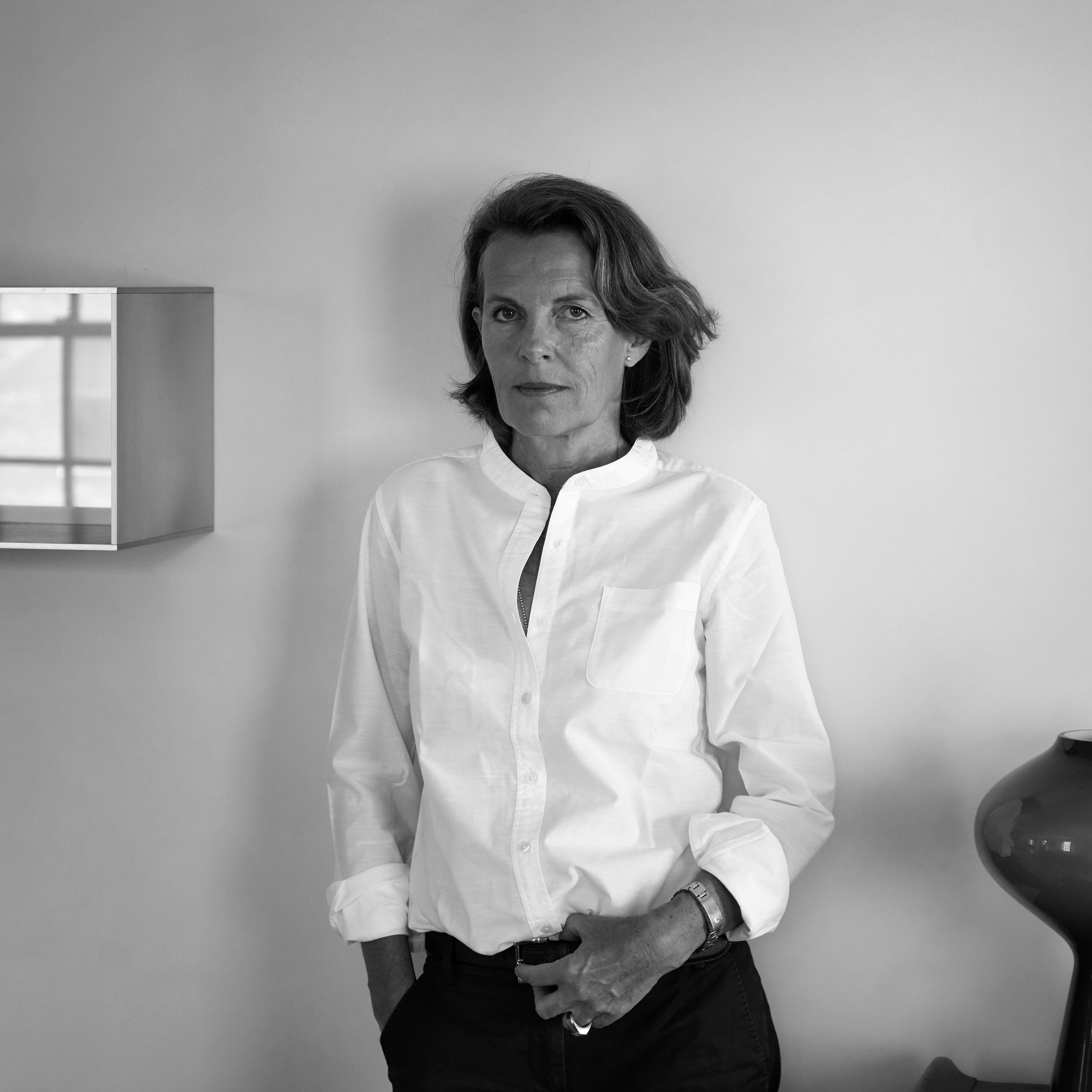 Black and white photograph of Annabelle Selldorf against a white wall with a few objects around her.