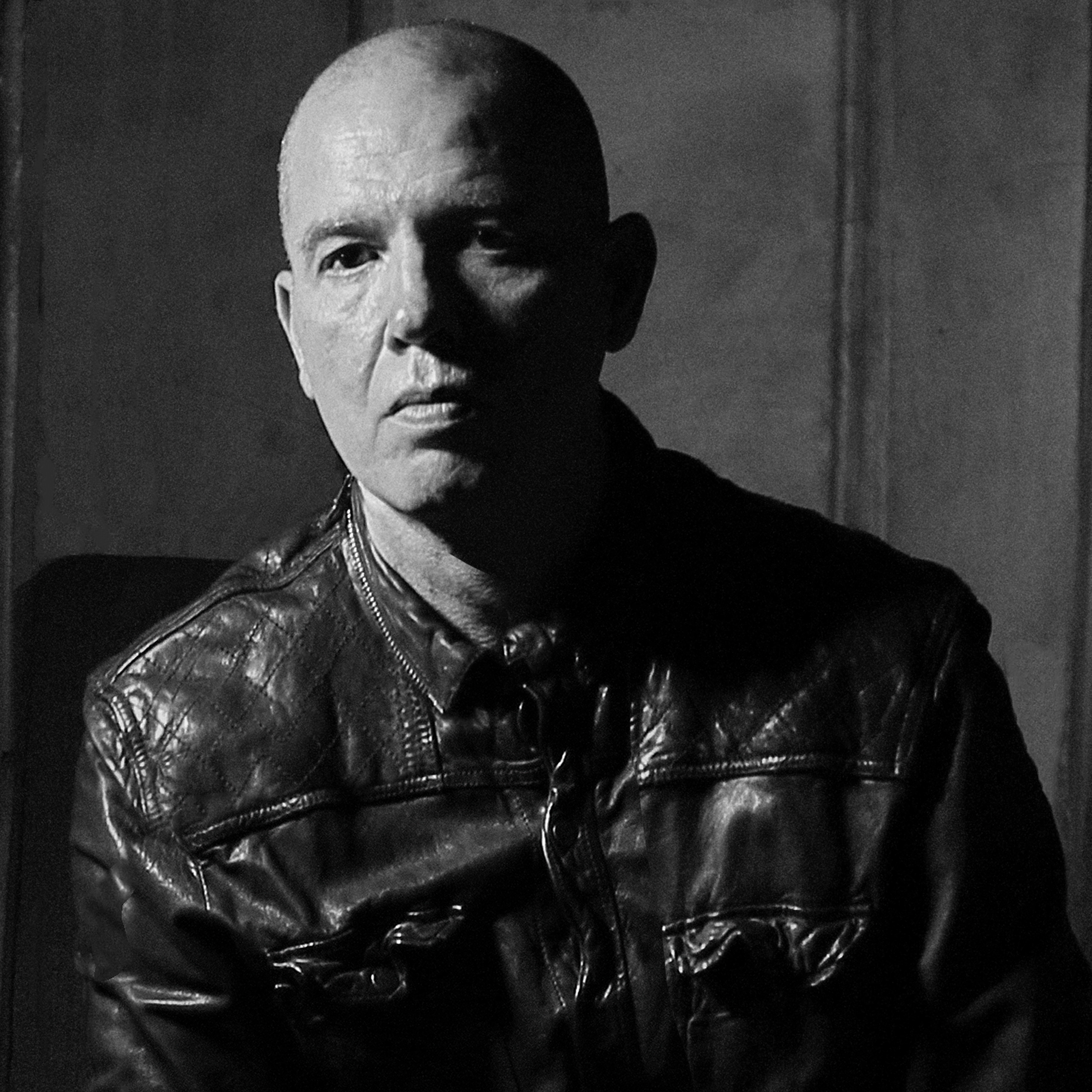 Black and white photo of Frank Franca wearing a leather jacket. Half of his face is covered by a shadow.