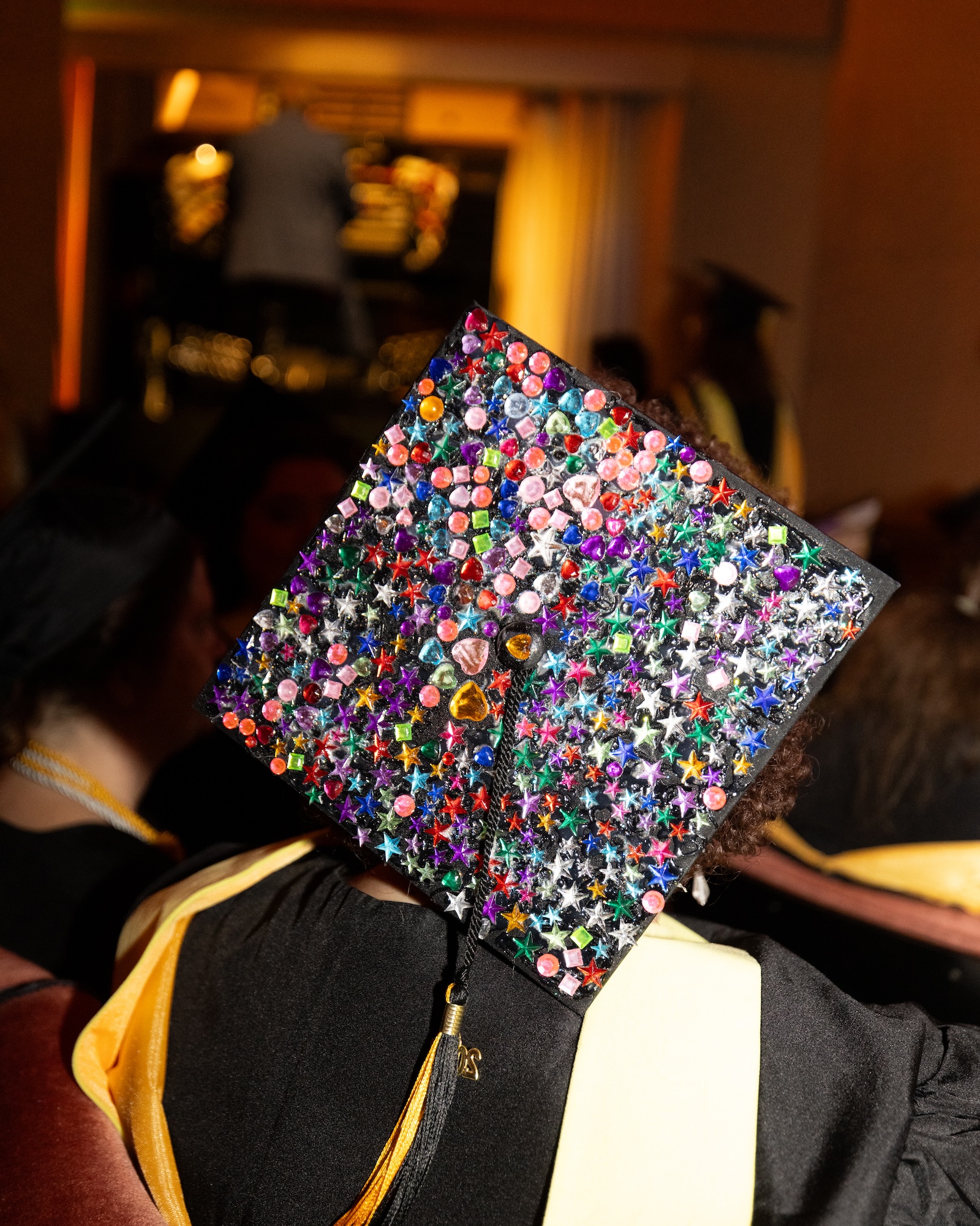 A graduation cap fully covered in colorful rhinestones and glittery star stickers.