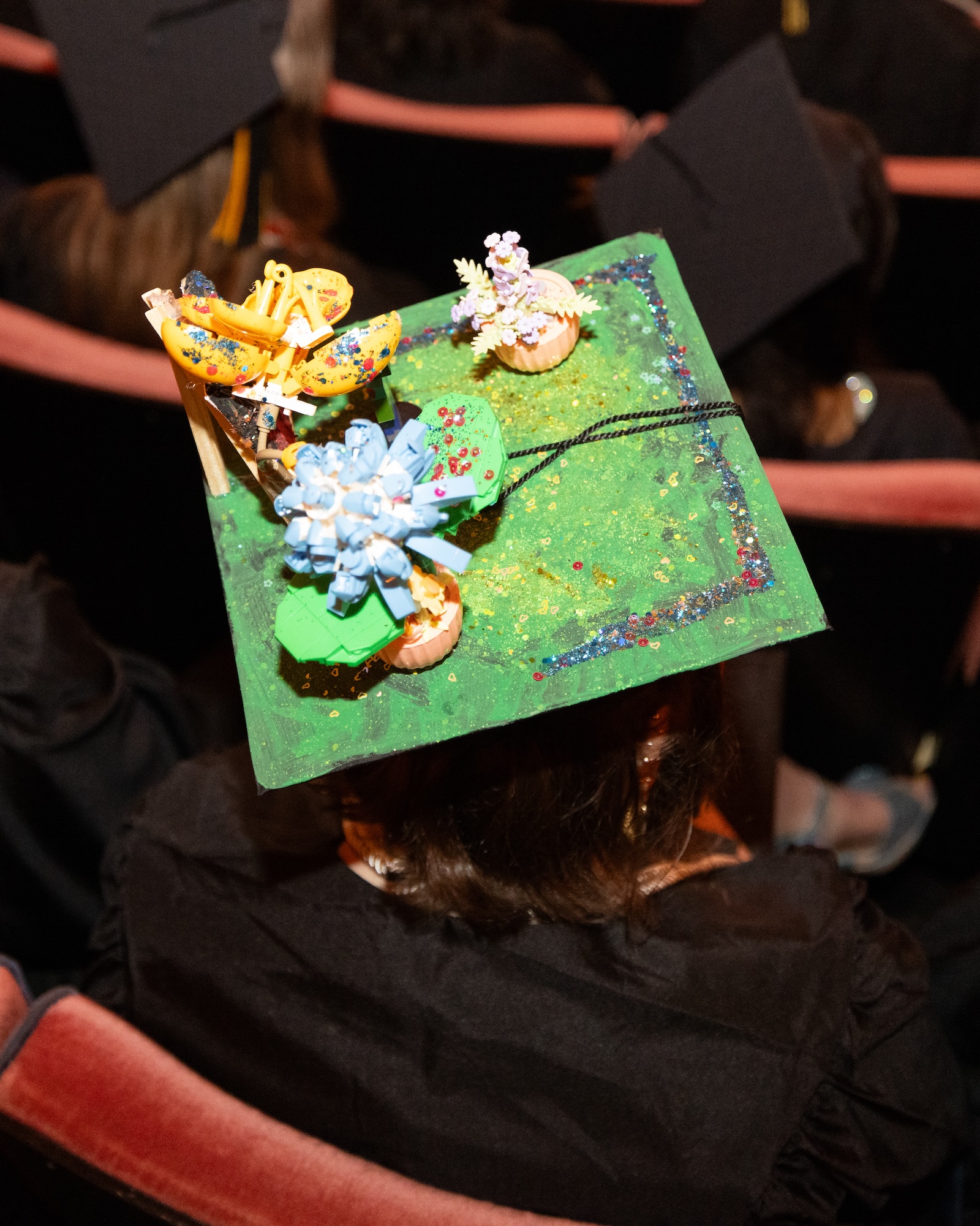 A graduation cap topped with miniature sculpted flowers, glitter, and three-dimensional decorative elements.