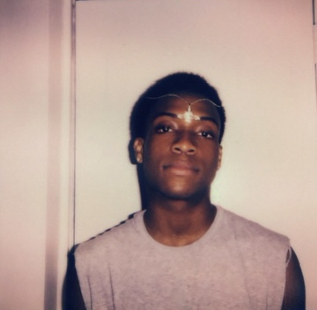 A Polaroid-style portrait of a young man wearing a sleeveless shirt, standing against a plain wall.