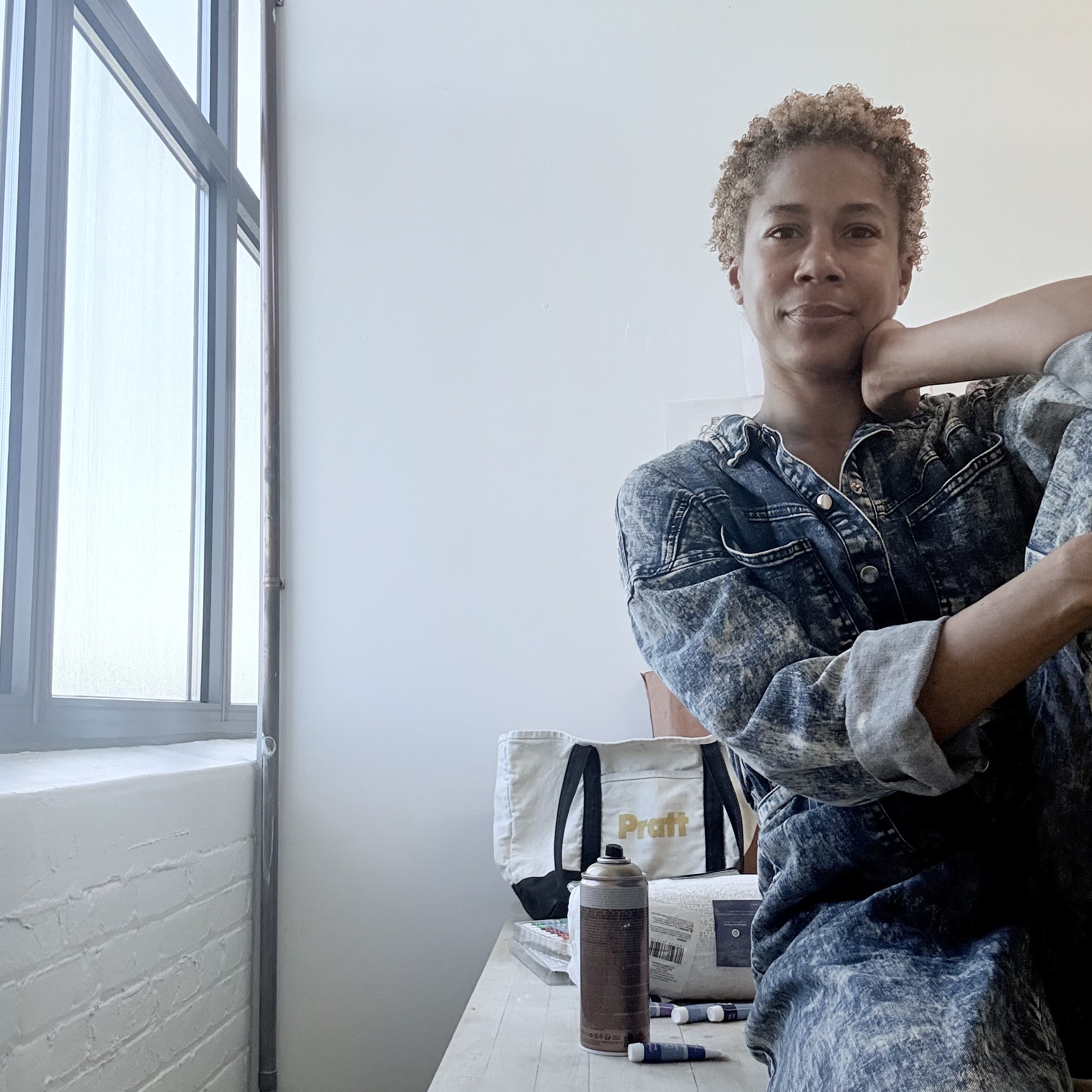 Student in denim clothing posing in a well-lit studio space near a window.