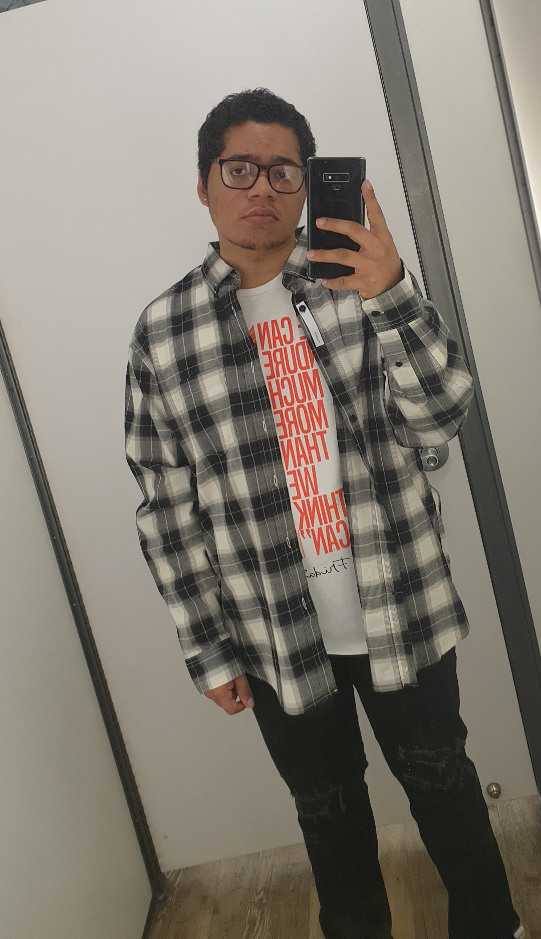 Student taking a mirror selfie wearing a plaid shirt and graphic tee.
