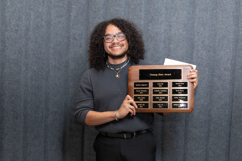Student smiling and holding a plaque for the “Unsung Hero Award”