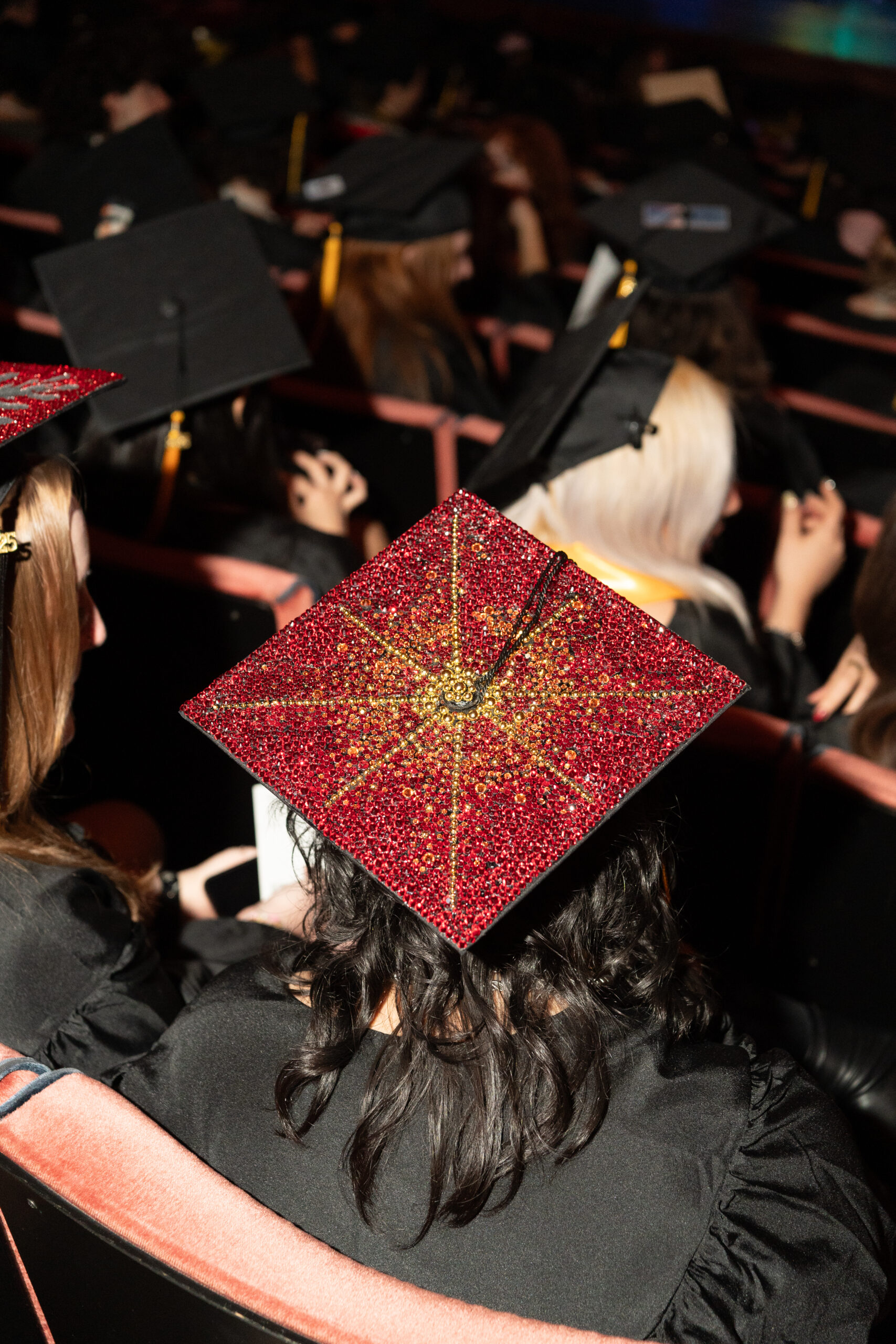 A graduation cap with red and yellow rhinestones in the shape of a sun or starburst