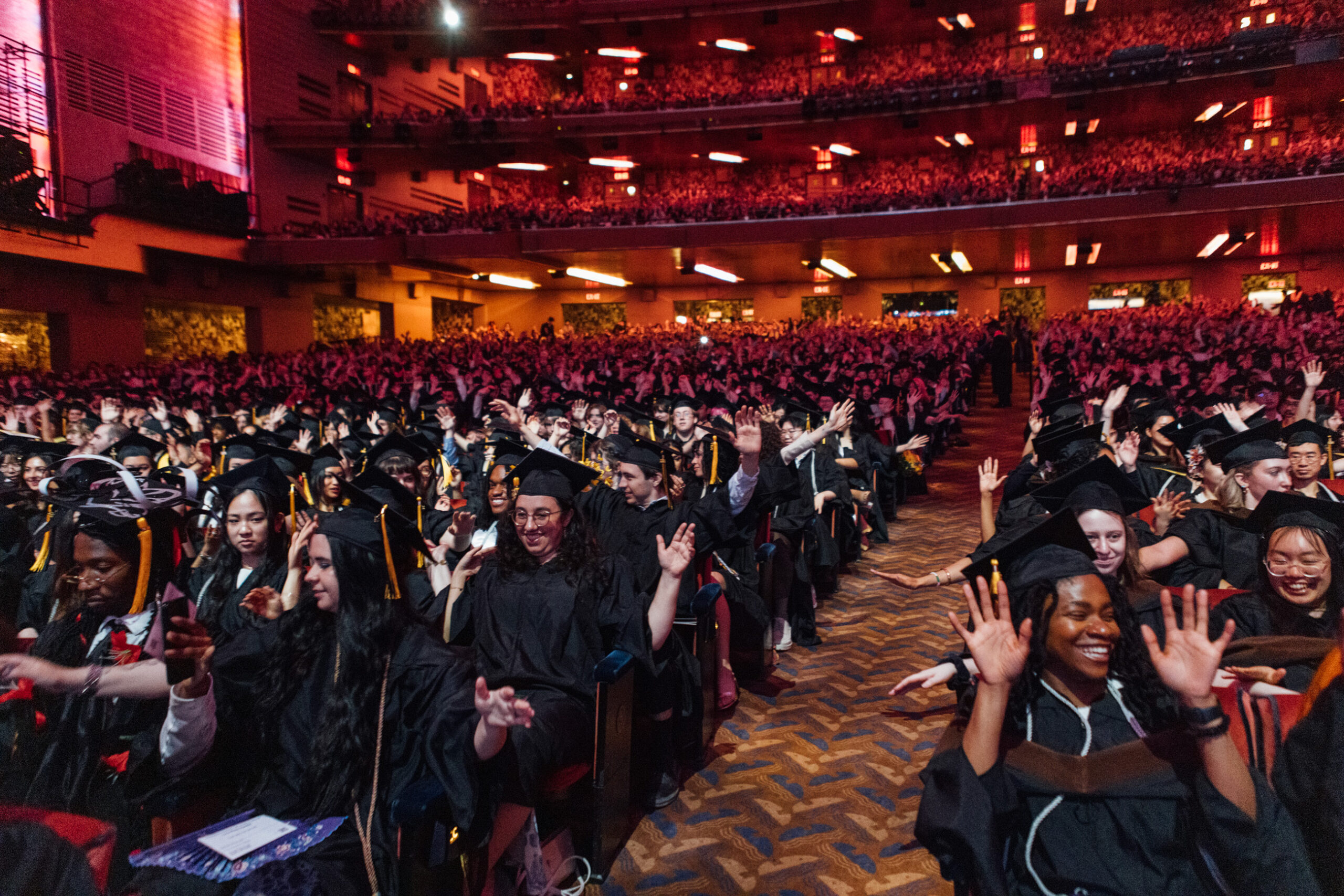 Pratt graduates in their caps and gowns attend the commencement ceremony at Radio City Music Hall. They are jubilant and smiling.