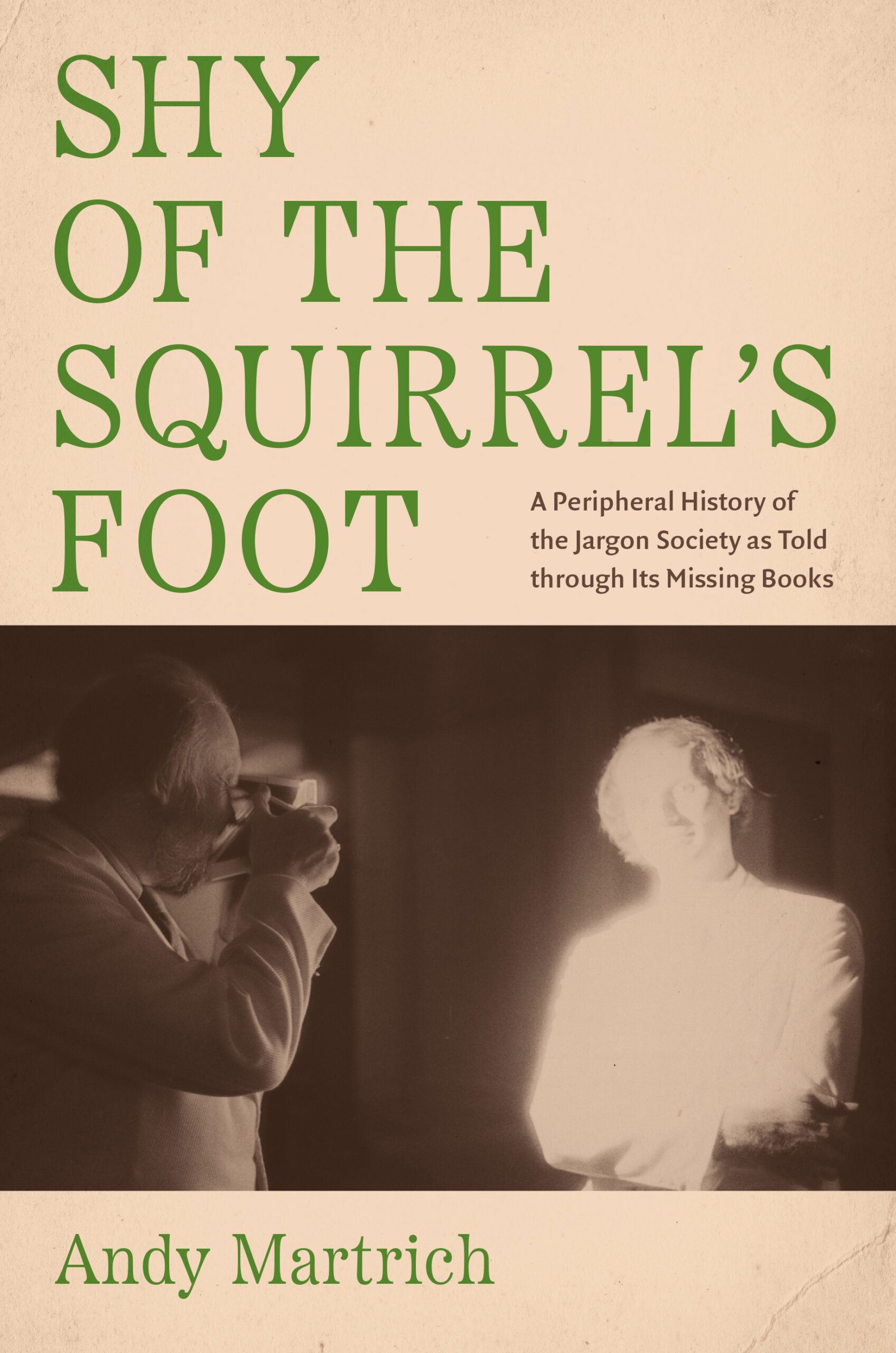 Beige book cover with the author’s name and title in green text; below, a sepia-toned image of two men, one of whom is photographing the other