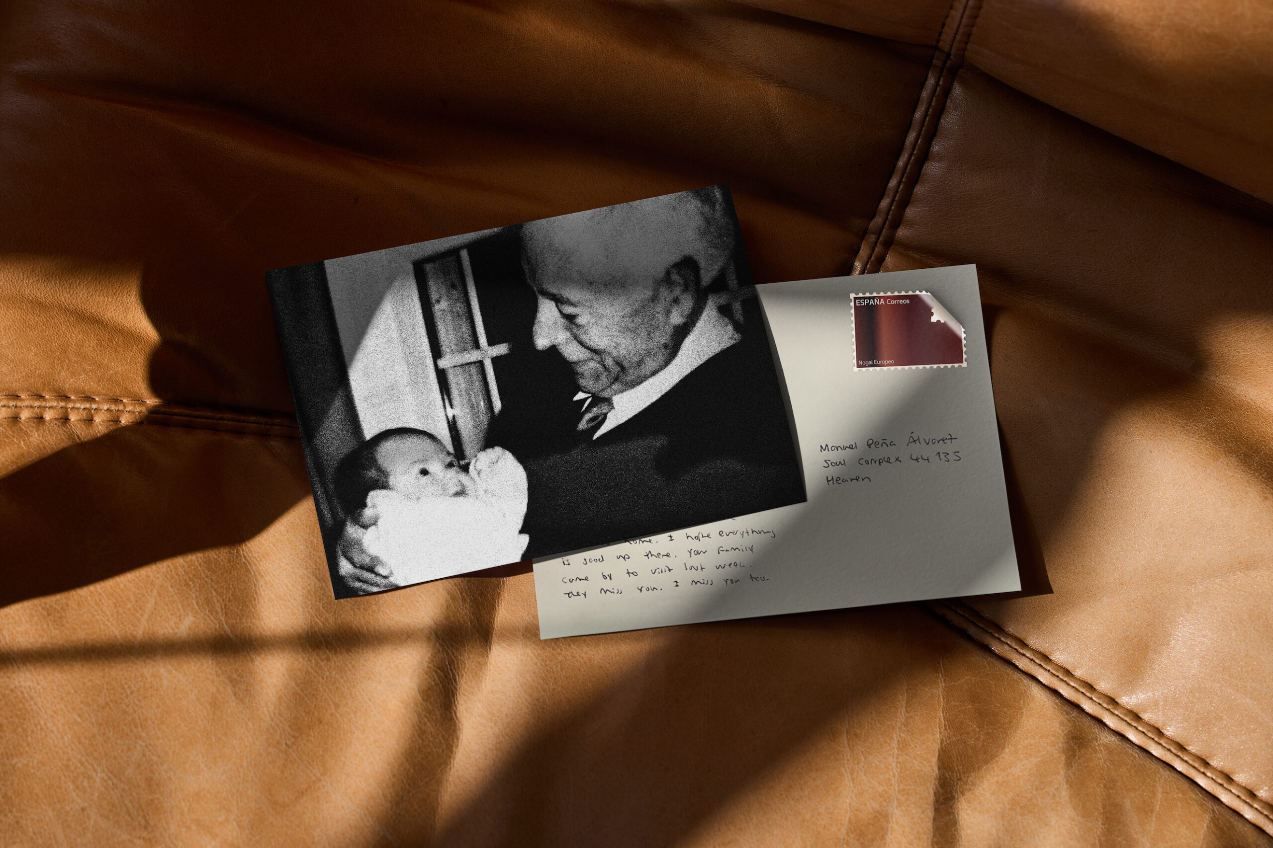 A black-and-white picture postcard showing a grandfather cradling his infant grandchild rests on another postcard with a handwritten note and brown stamp.