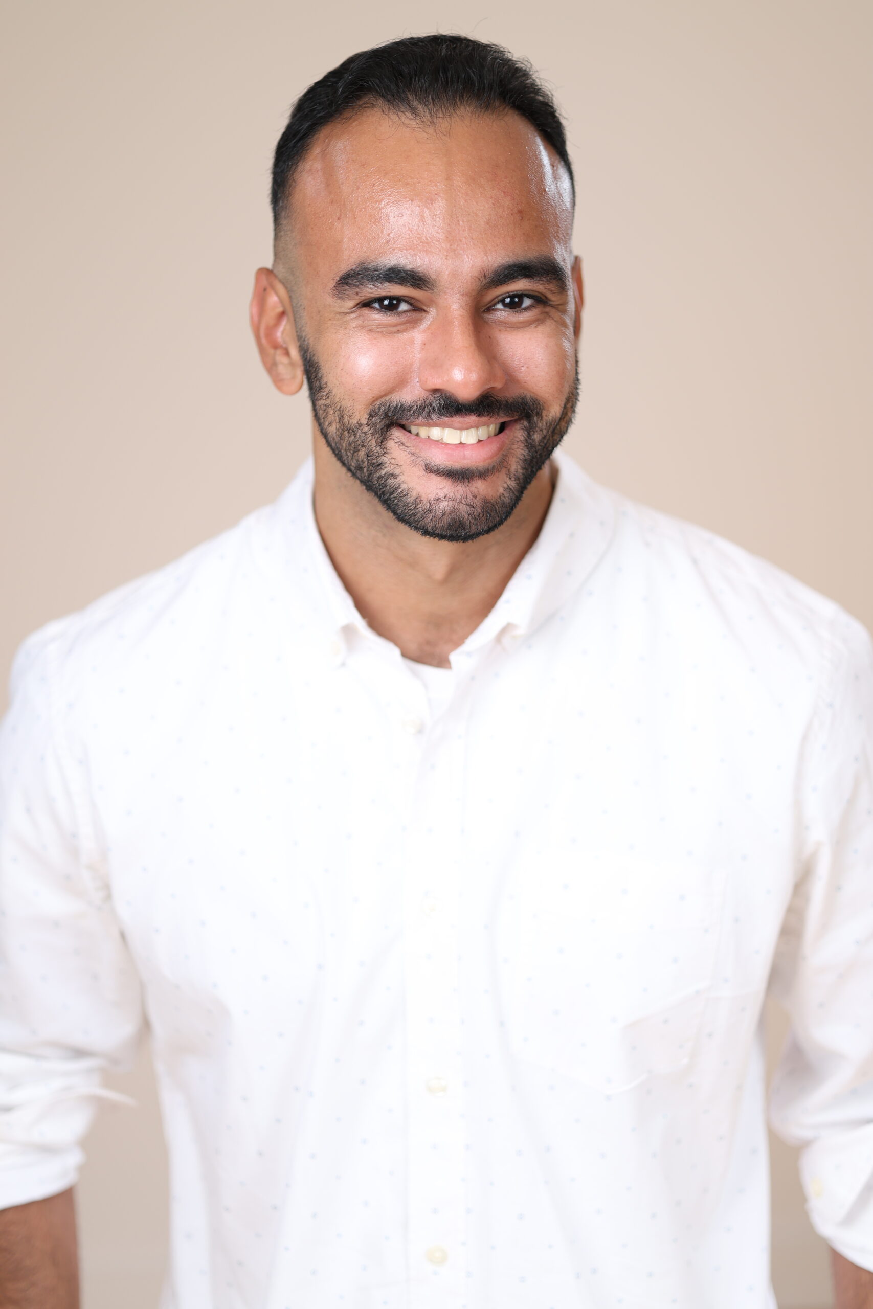 Headshot of Sebastian Torrens, wearing a white button down and smiling at the camera in front of a tan background