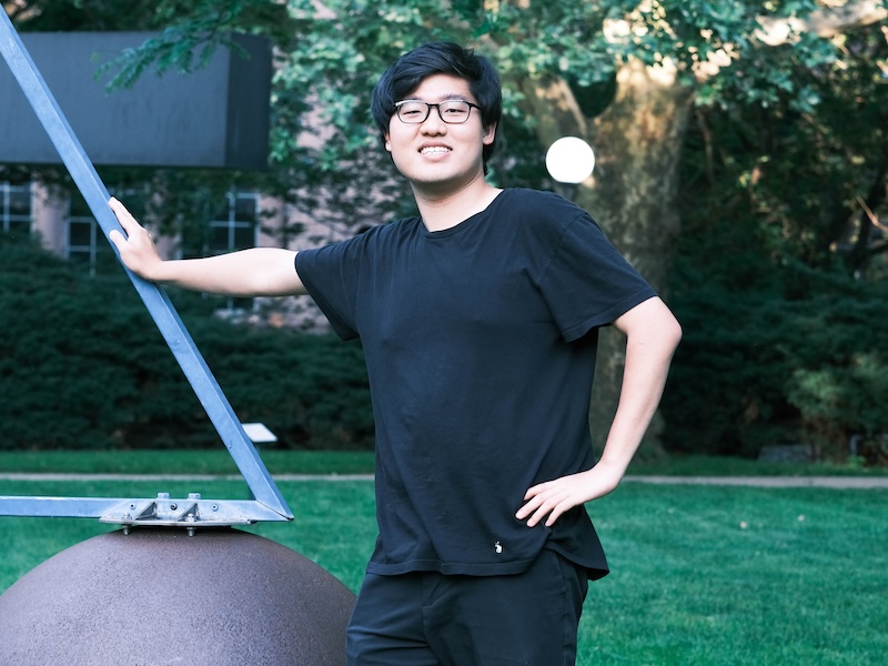Student in a black outfit posing outdoors near a metal sculpture on campus.