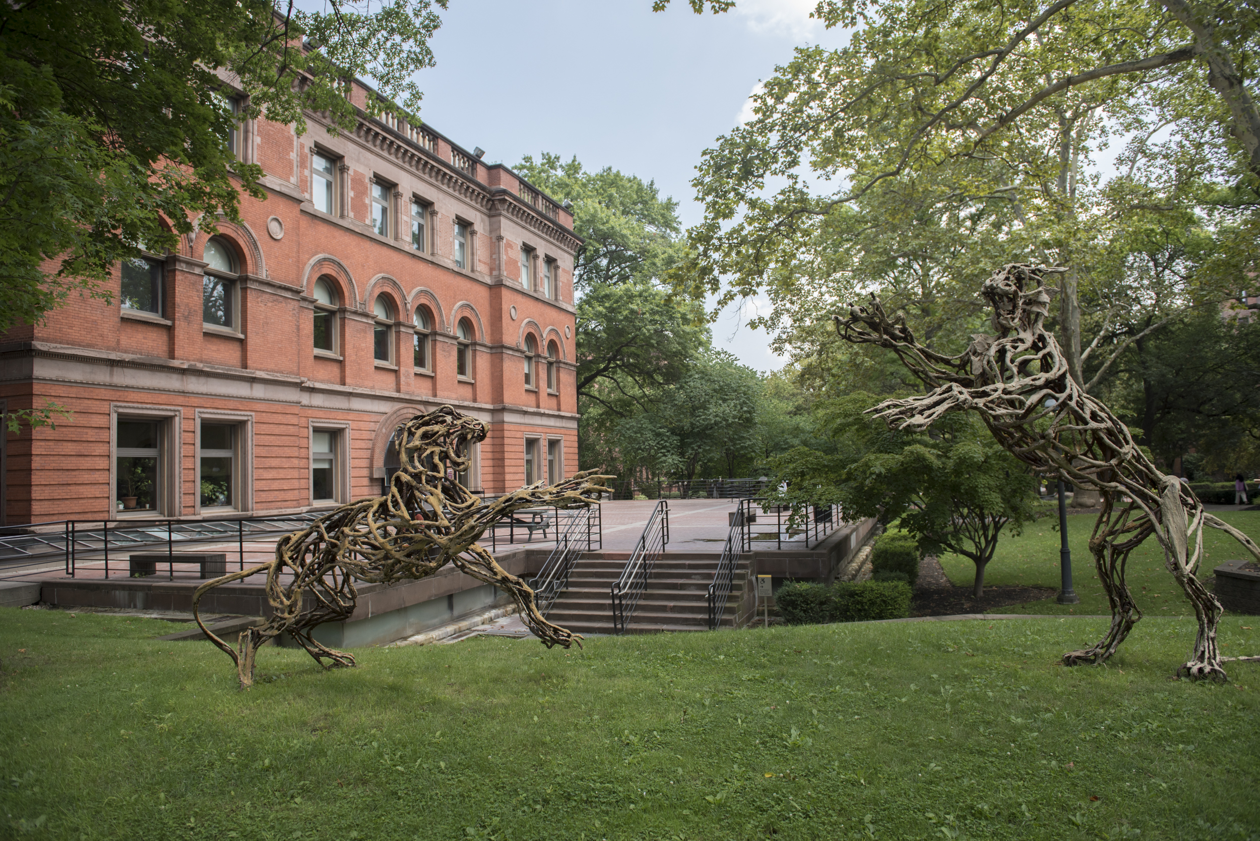 Image of Pratt Institute's Brooklyn Campus - a wooden sculpture of two large wildcats in the foreground, the Pratt Library in the background.