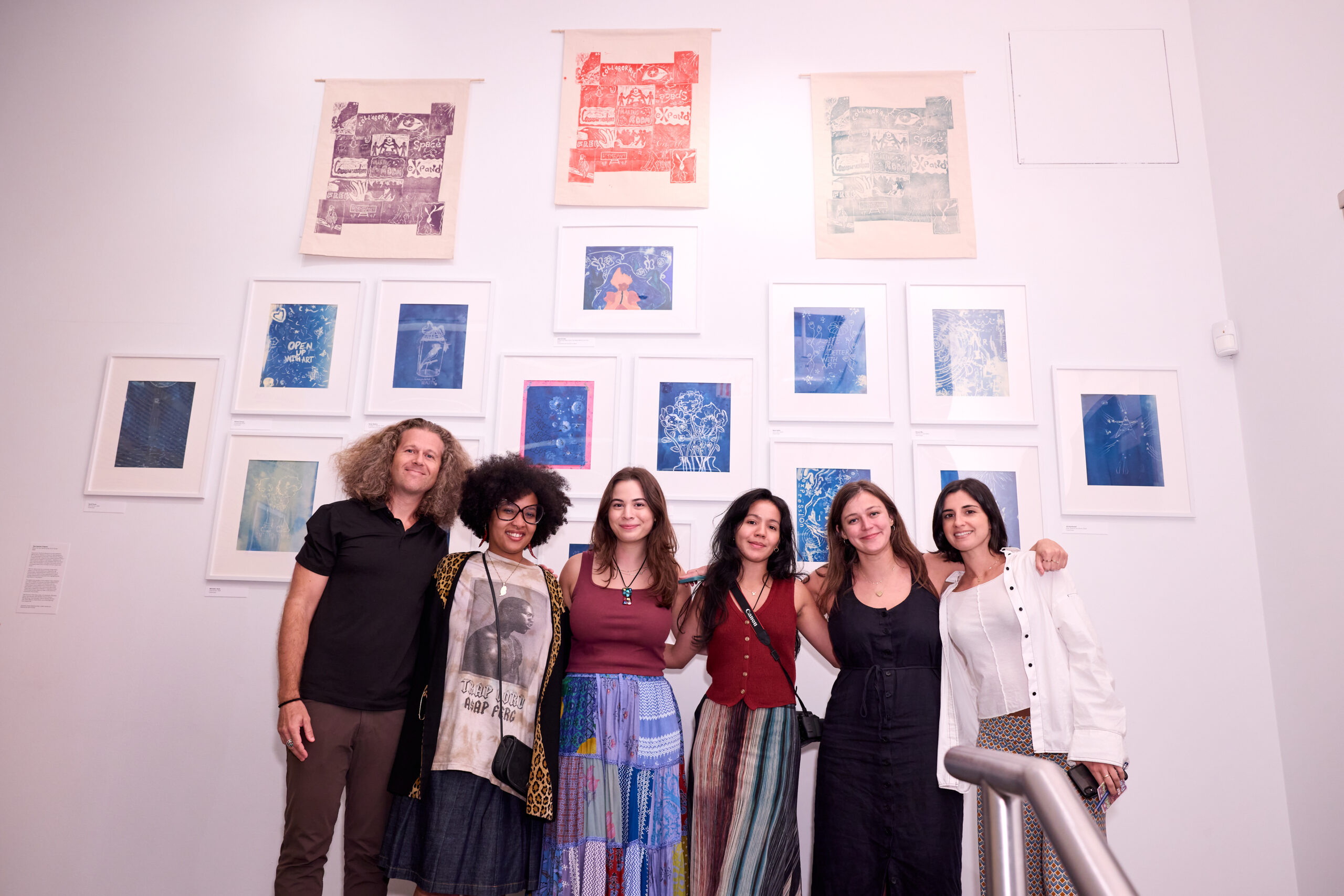 Six people smile in front of a wall of art prints.