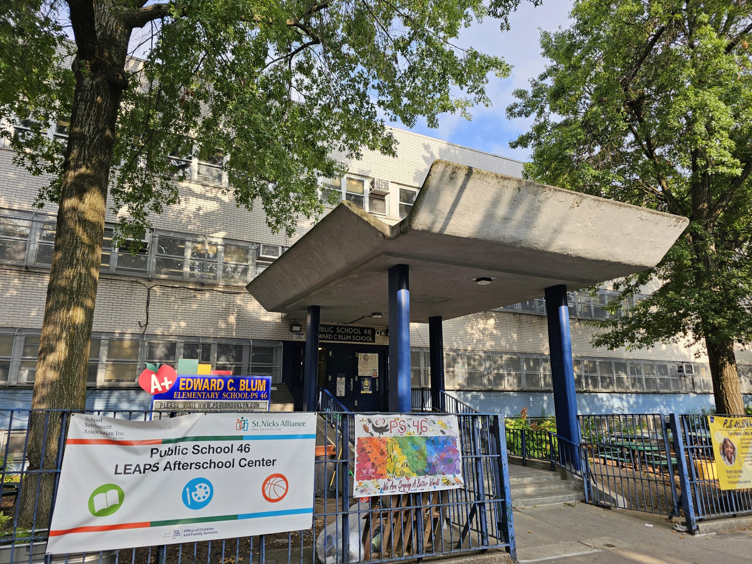 The front of a public school, with colorful signs and trees with green leaves.