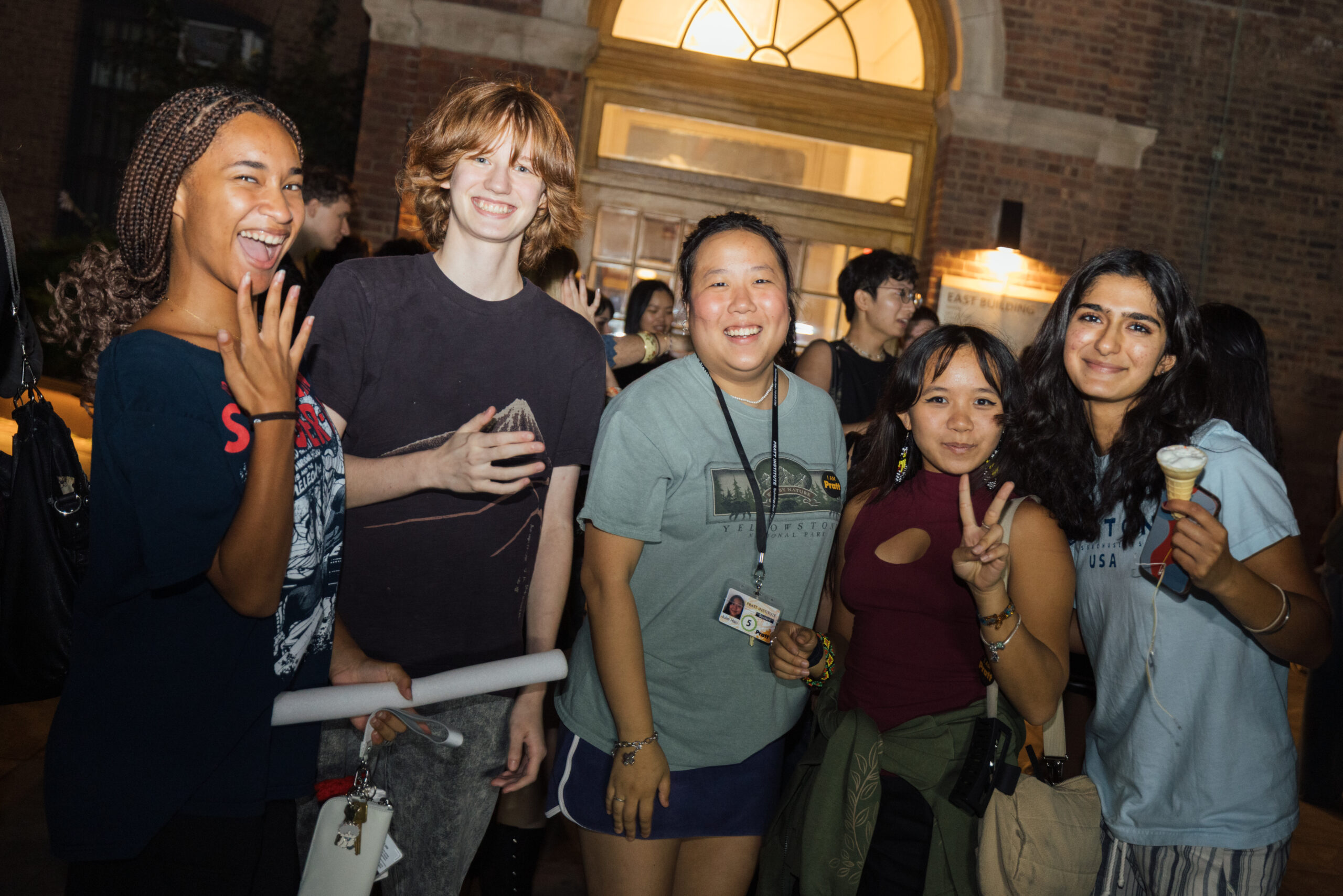 Smiling students pose for a photo in the nighttime as the light from a building in the background illuminates the scene.