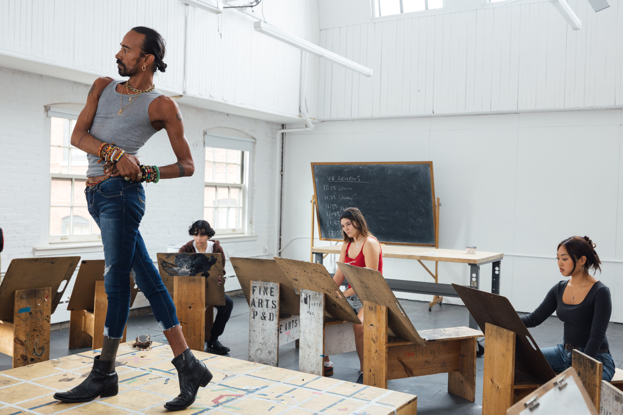 Sunlight pours into a spacious room as students with easels engage in a live drawing session as the model poses on a raised platform.