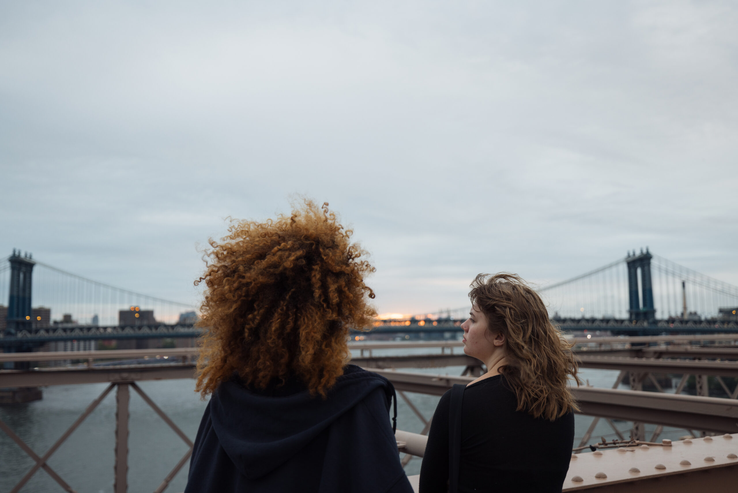 Two students stand on the Brooklyn bridge gazing at the sunrise.
