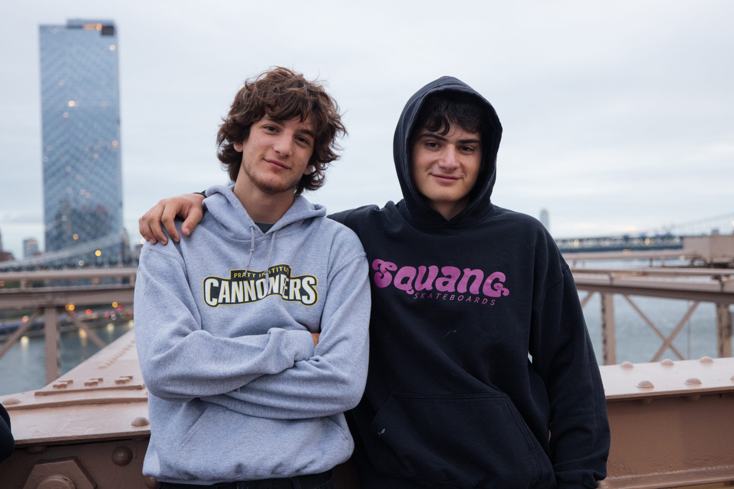 Two young men pose for a photo on the Brooklyn Bridge in early morning.