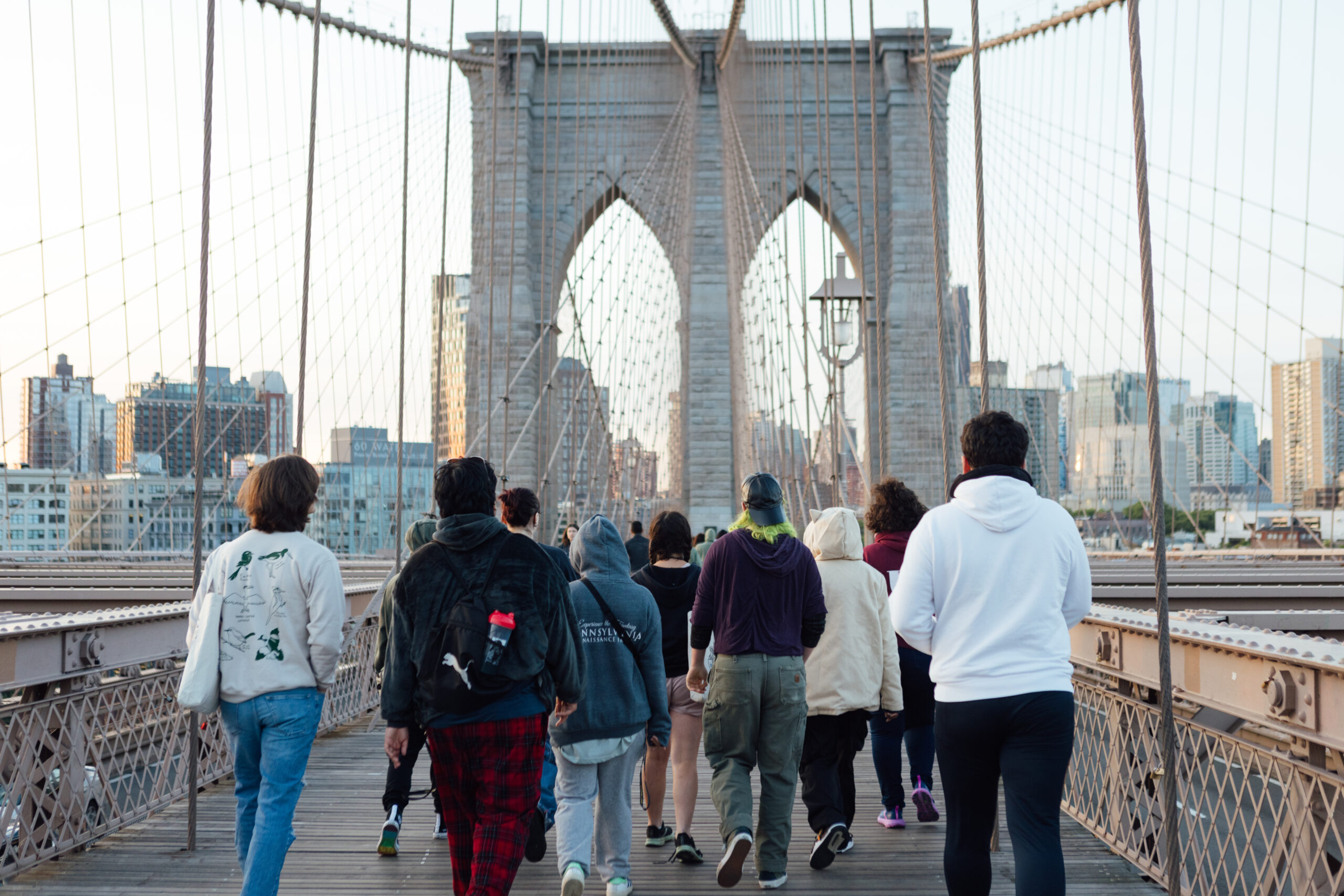 A group of people, seen from behind, walking over the Brooklyn Bridge.