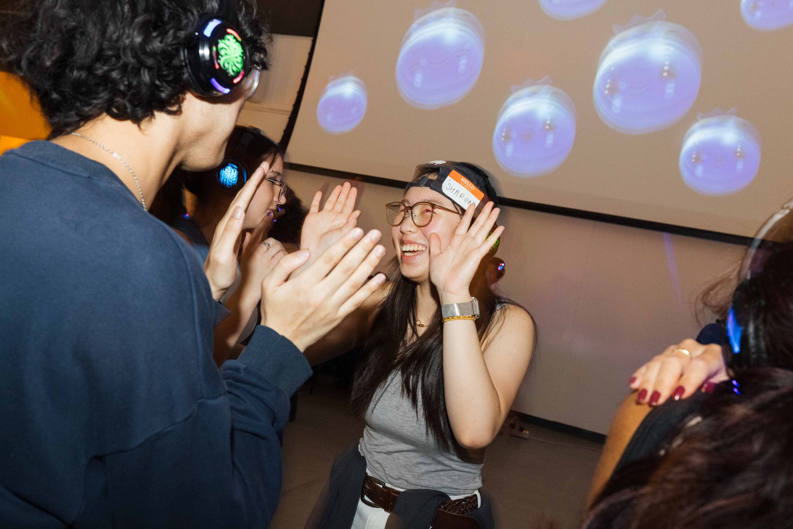 College students wearing over-the-head headphones and dancing with their hands up.