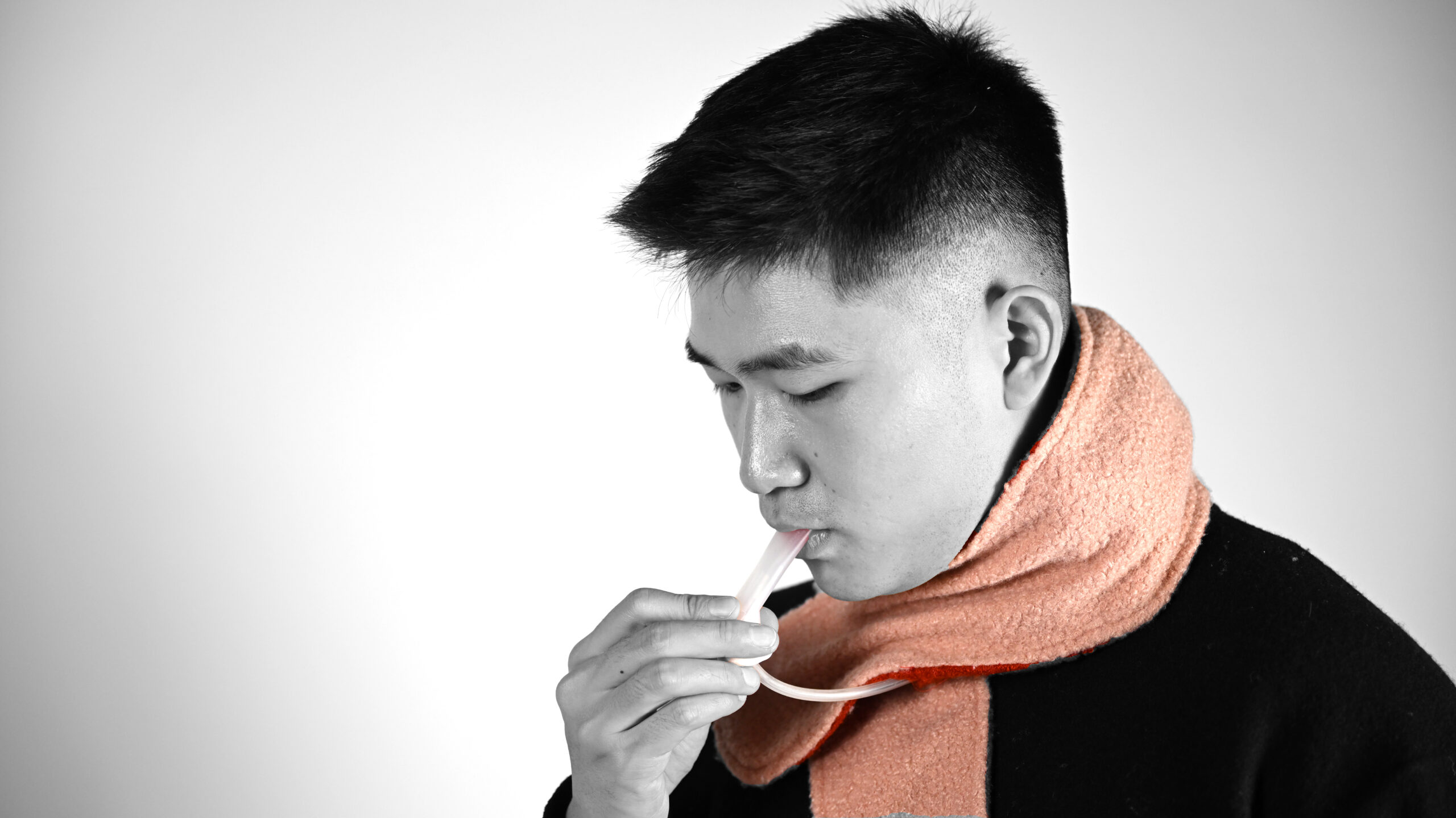 A person blows into a straw attached to a pad wrapped around their neck.
