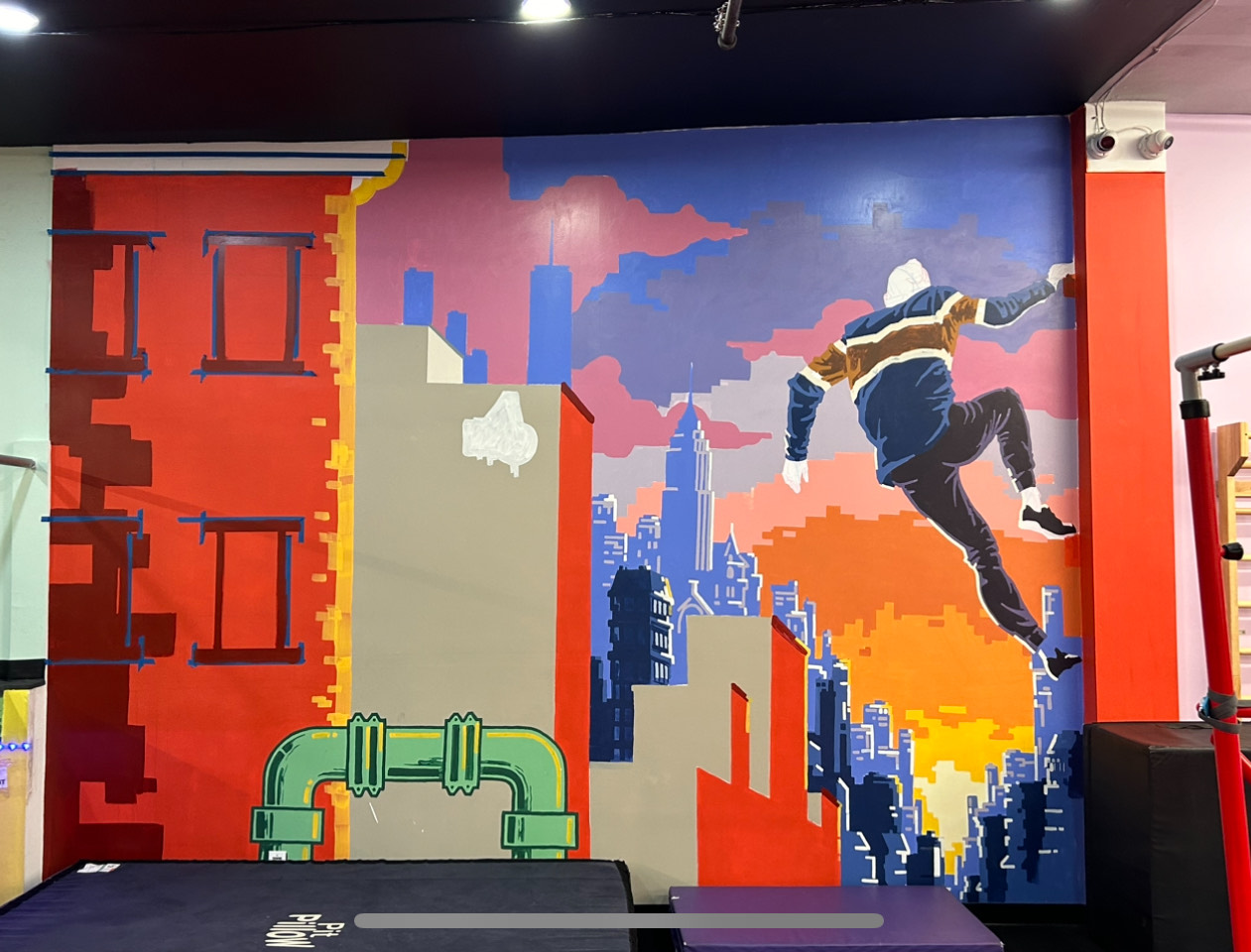 A vivid mural of a person leaping between city rooftops at sunset, set against a stylized skyline in bold red, blue, and purple tones.