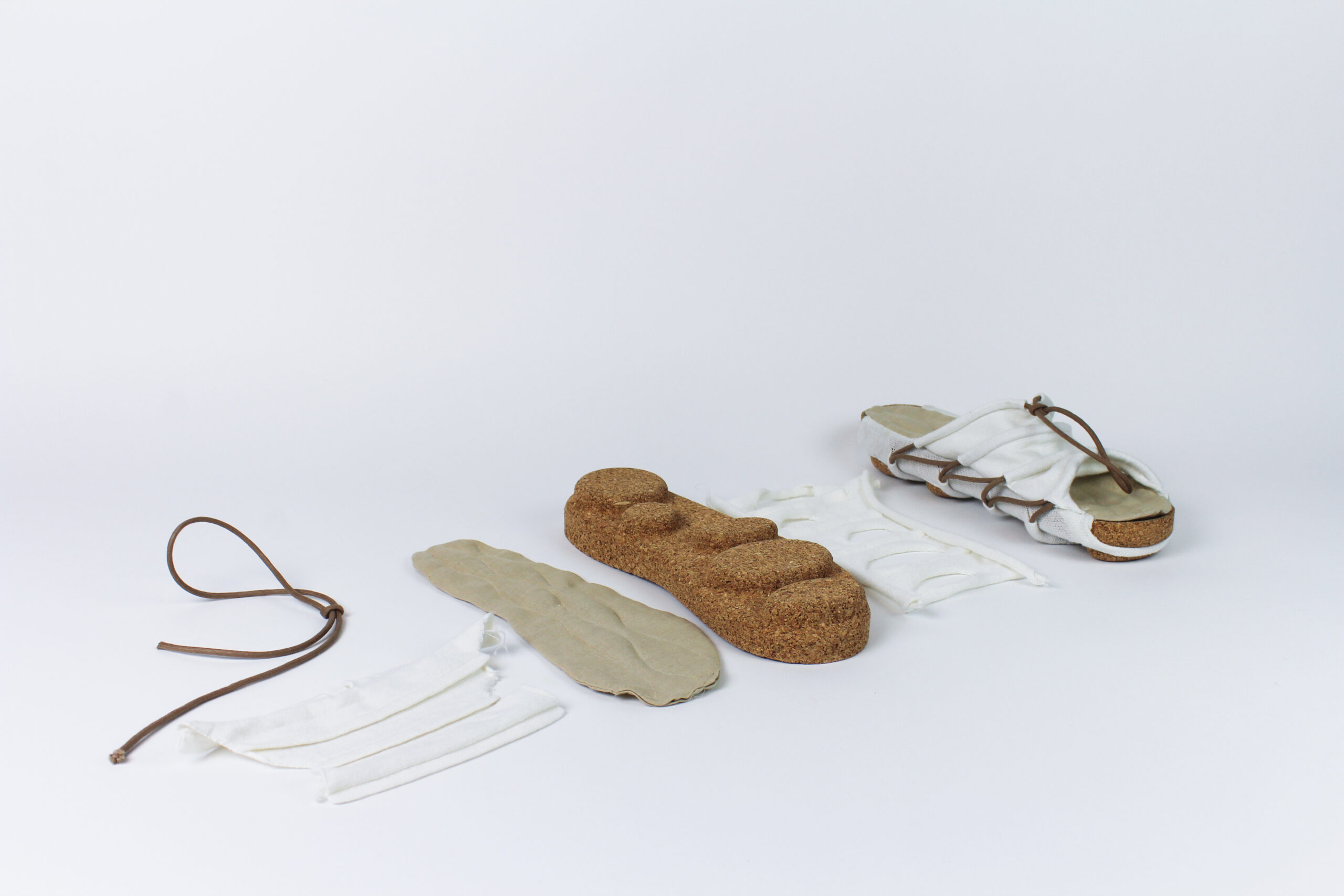 Deconstructed view of a modular sandal laid out in parts, including cork sole, fabric upper, leather laces, and inner padding, displayed on a white surface.