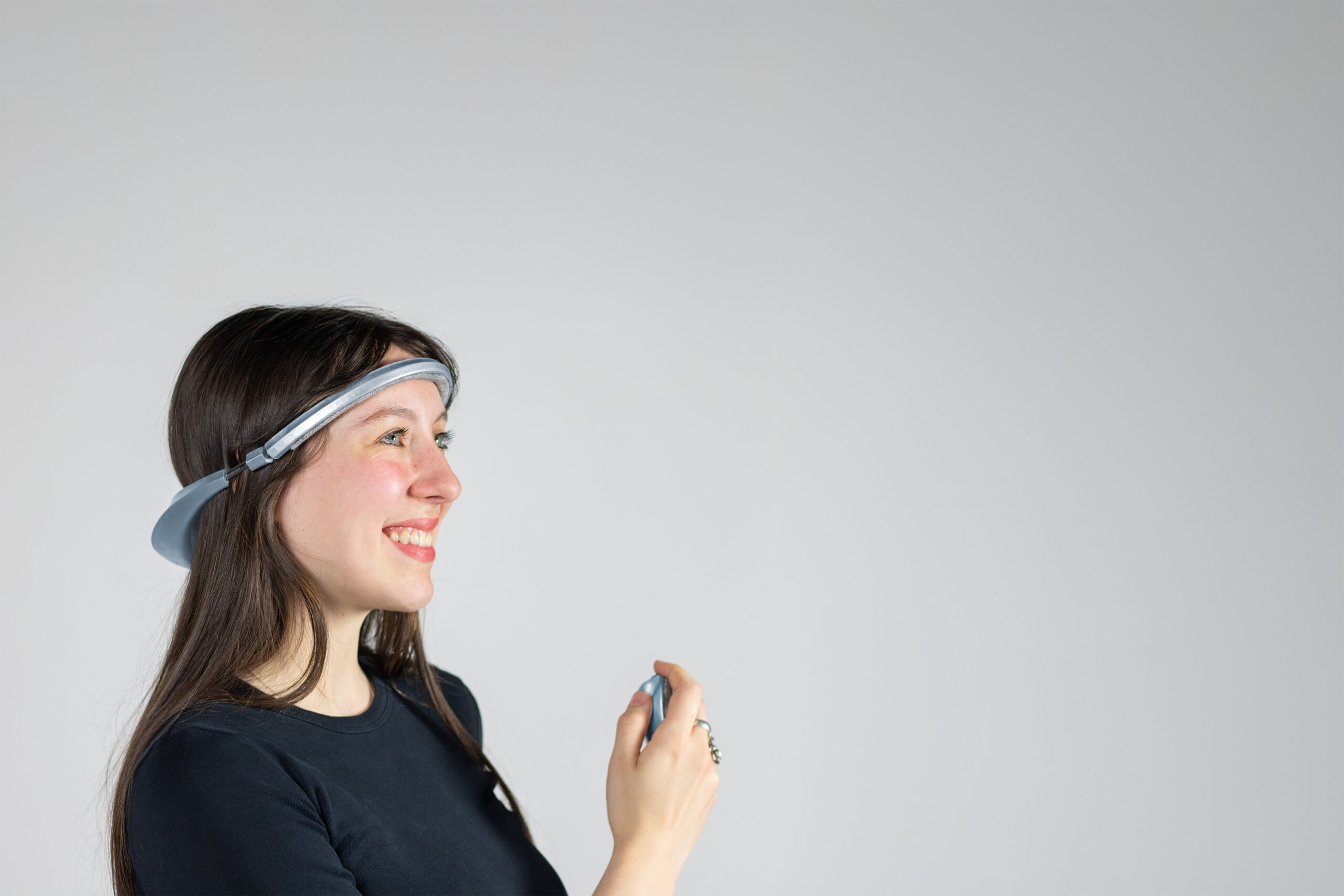 A smiling woman wears a tech band around her head and holds a corresponding device as she looks into the distance.