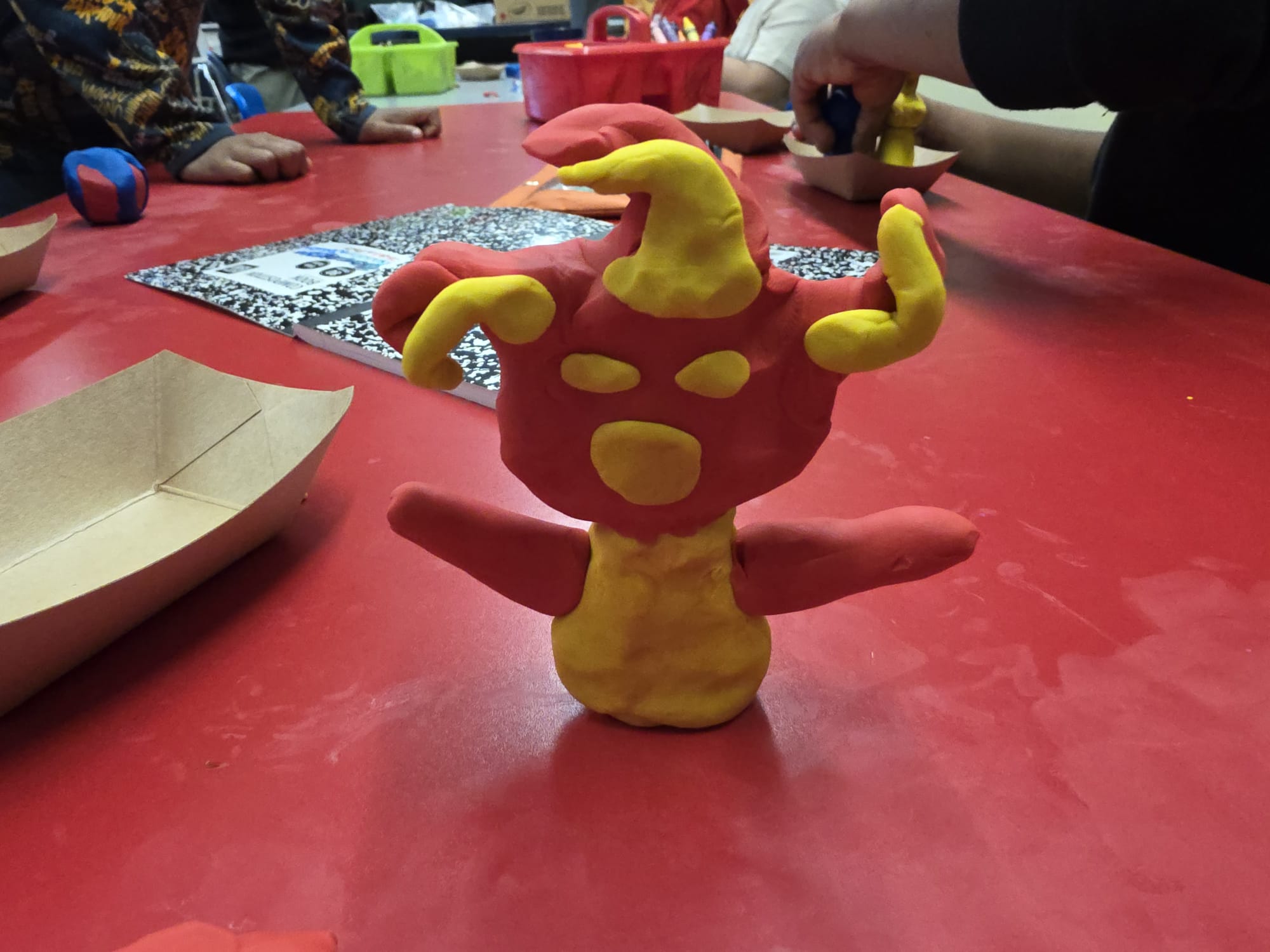 A red and yellow clay creature sitting on a red table.