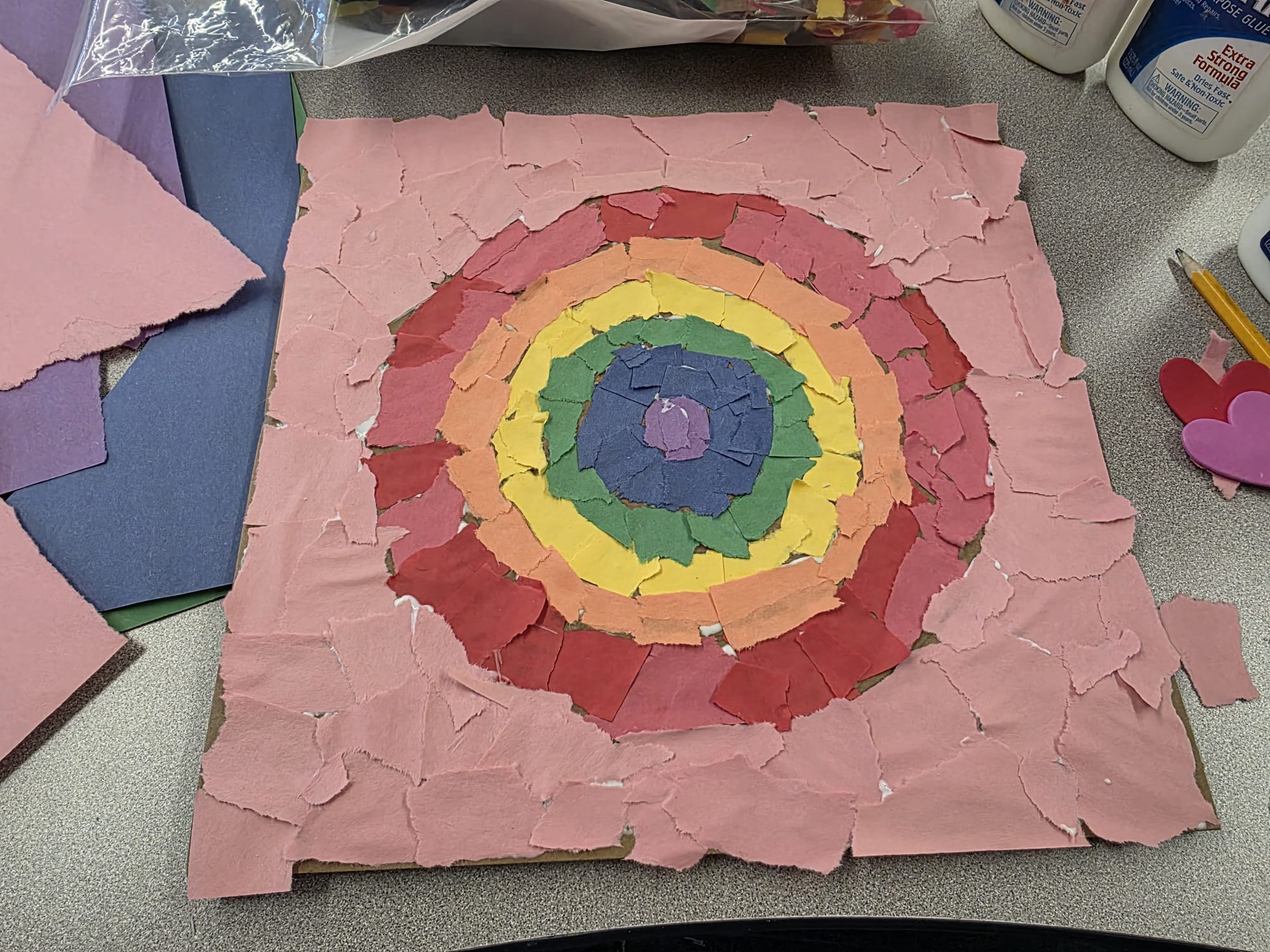 A collage of ripped up construction paper that creates concentric circles of rainbow colors.