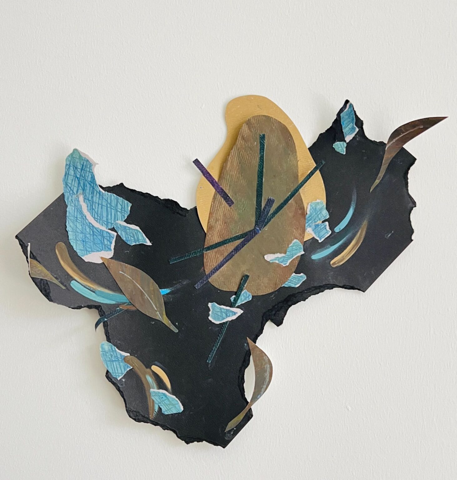 A mixed-media collage on black paper featuring an abstract golden oval form surrounded by torn blue paper fragments, metallic shapes, and layered cutouts. The composition has a fragmented quality with flowing, organic lines against the dark background.