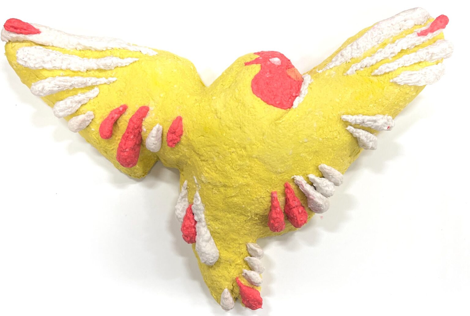 A painted papier-mâché sculpture of a bird with wings outstretched. The bird is yellow with bright red and white accents on its wings, tail, and head, emphasizing a stylized, decorative design.