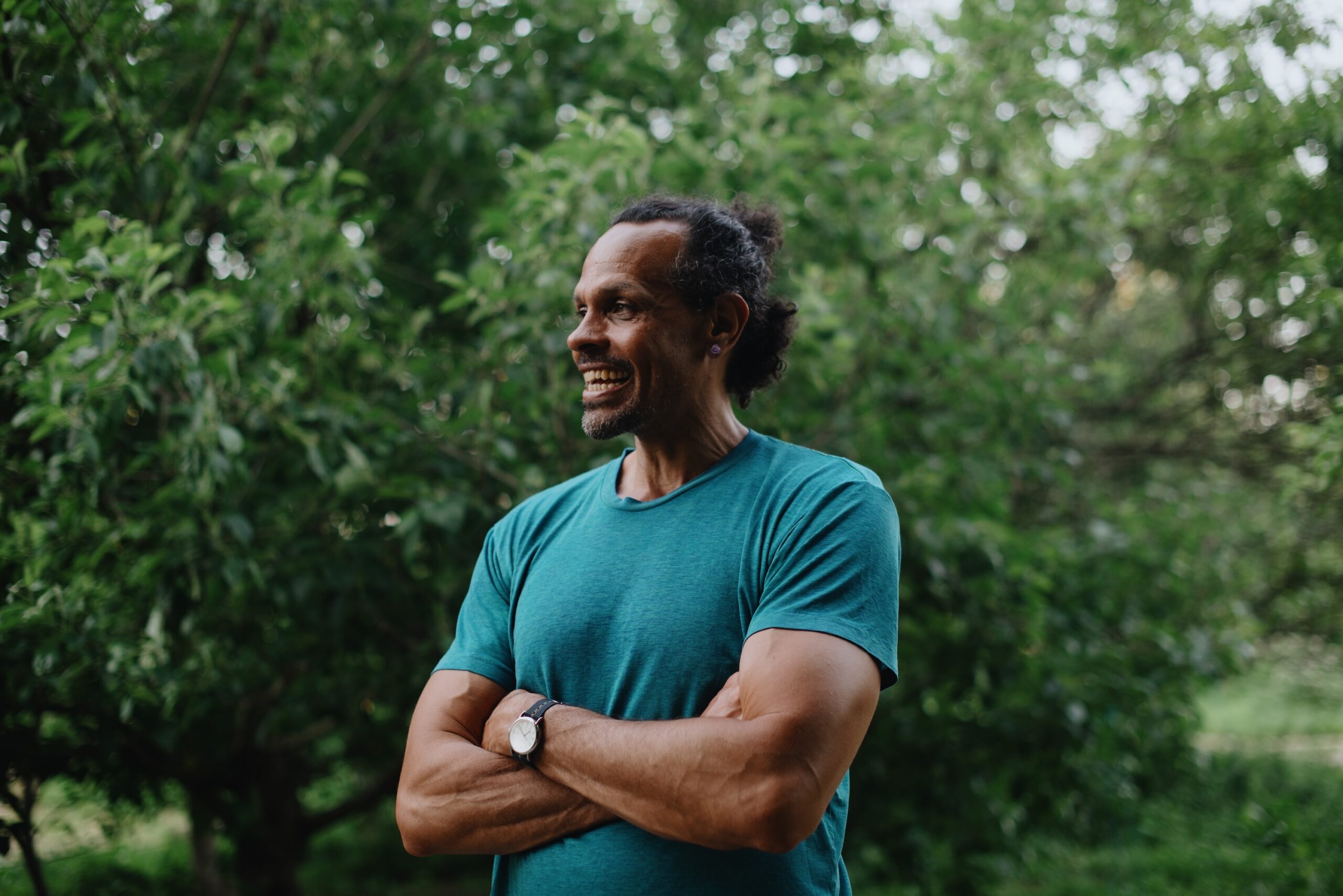 Ross Gay stands in front of trees wearing a blue shirt