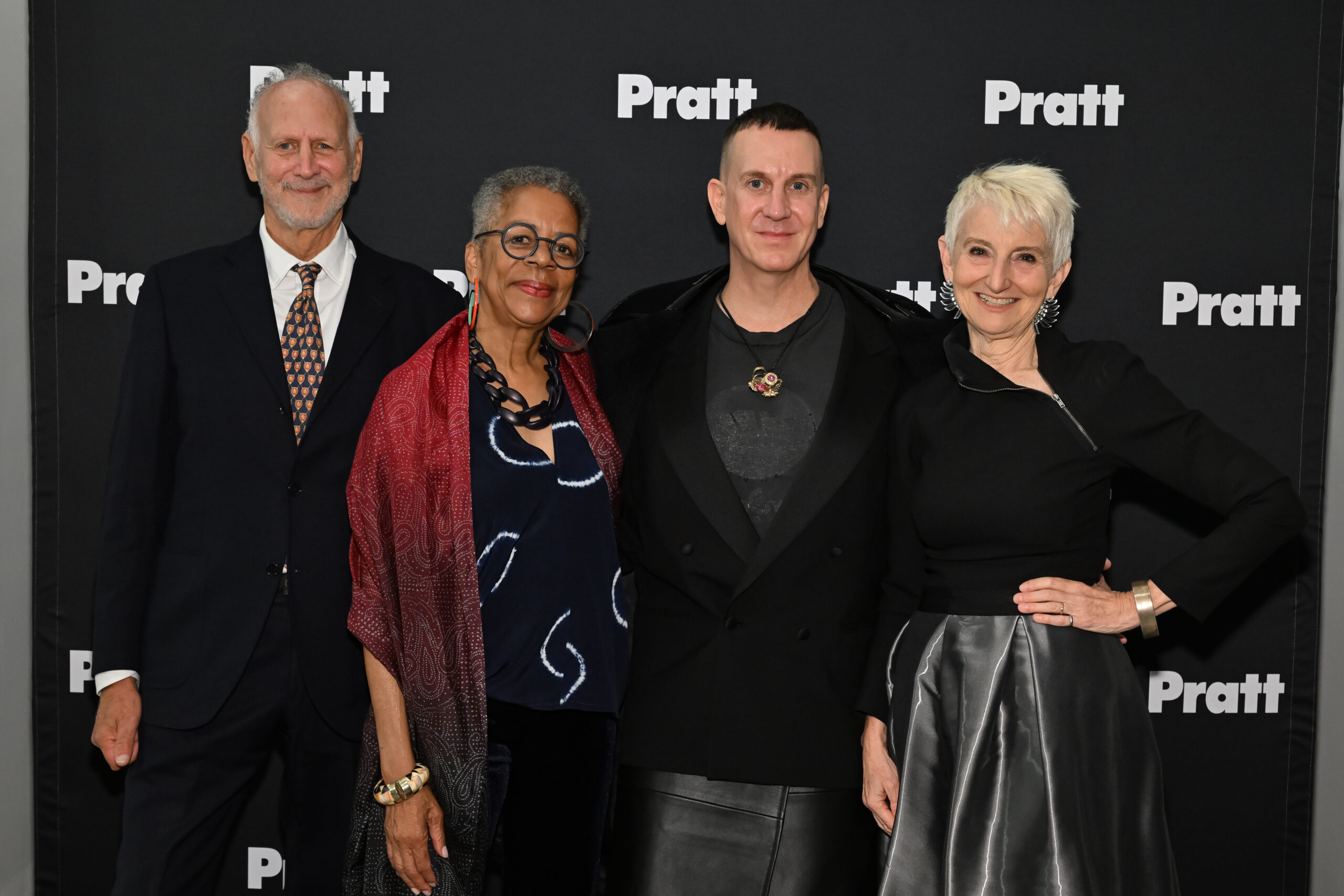 Four individuals pose together in front of a black backdrop featuring the word 