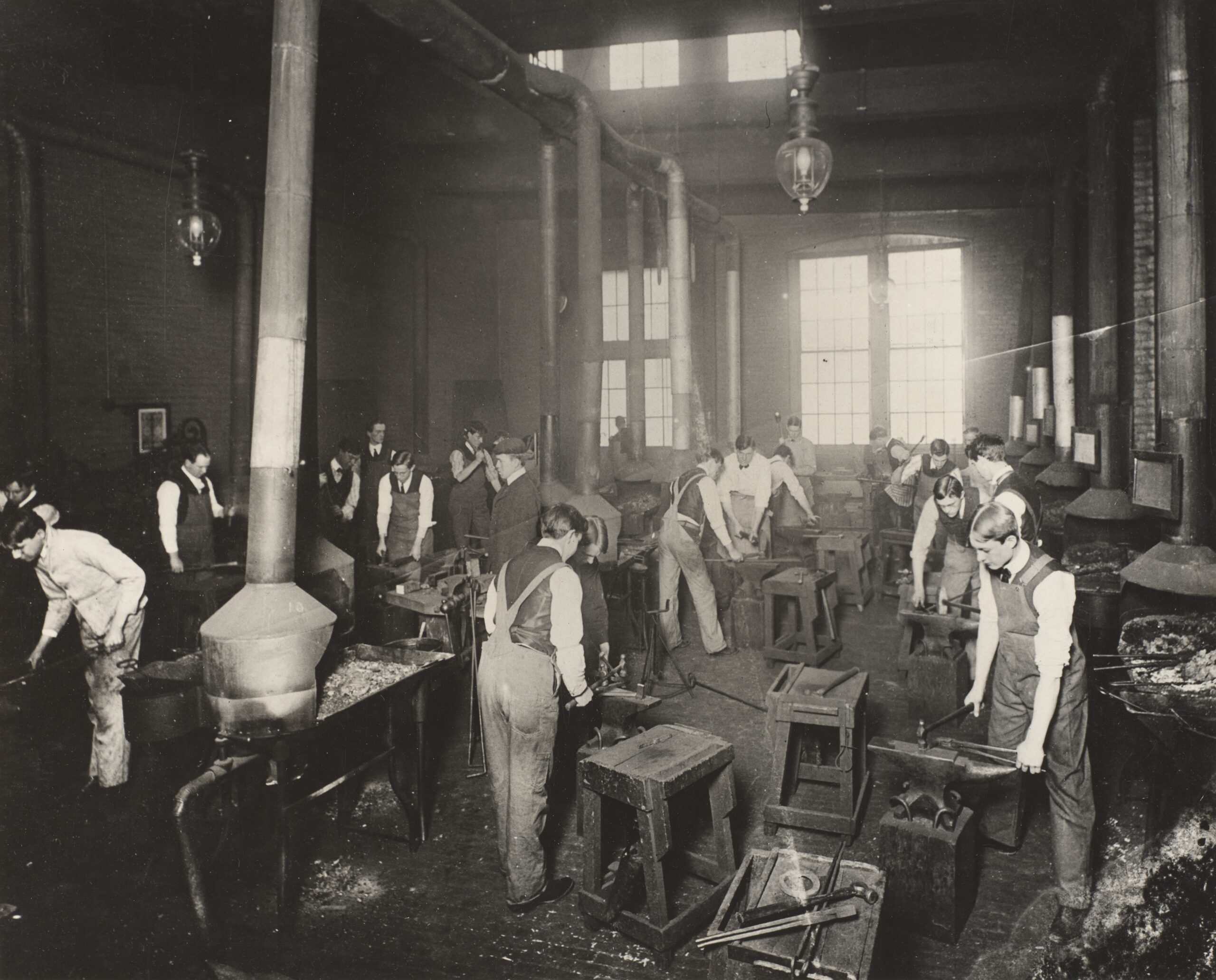 A large group of engineering students forge metalwork around the turn of the 20th century.