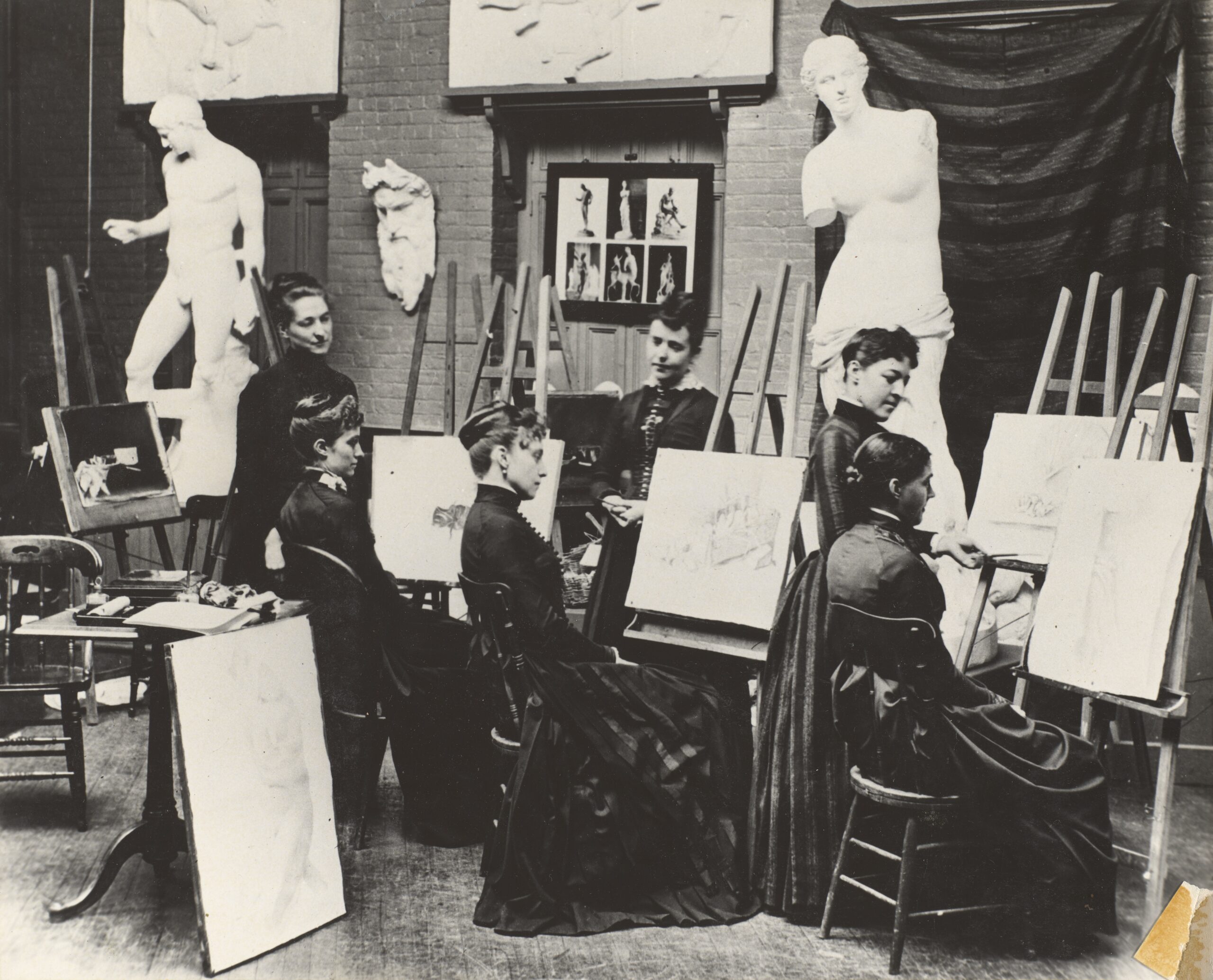 Students in a drawing studio sketch the classical statues in front of them around the turn of the 20th century.