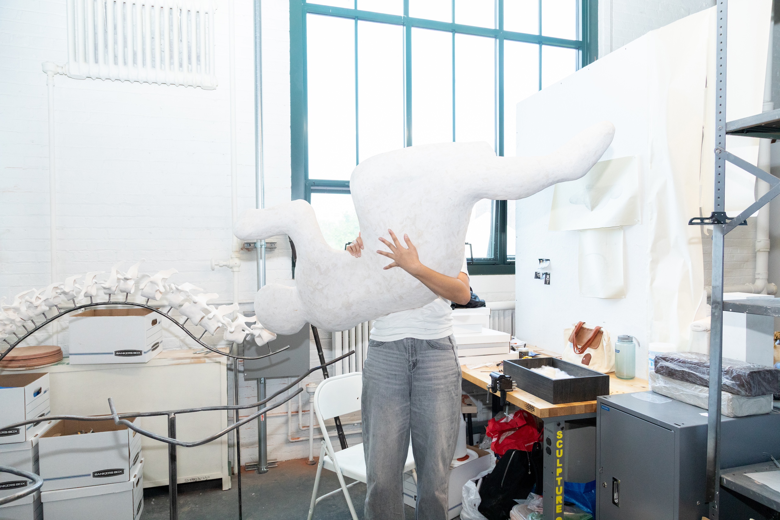 A person is holding a large, white sculptural figure that resembles a human in a studio.