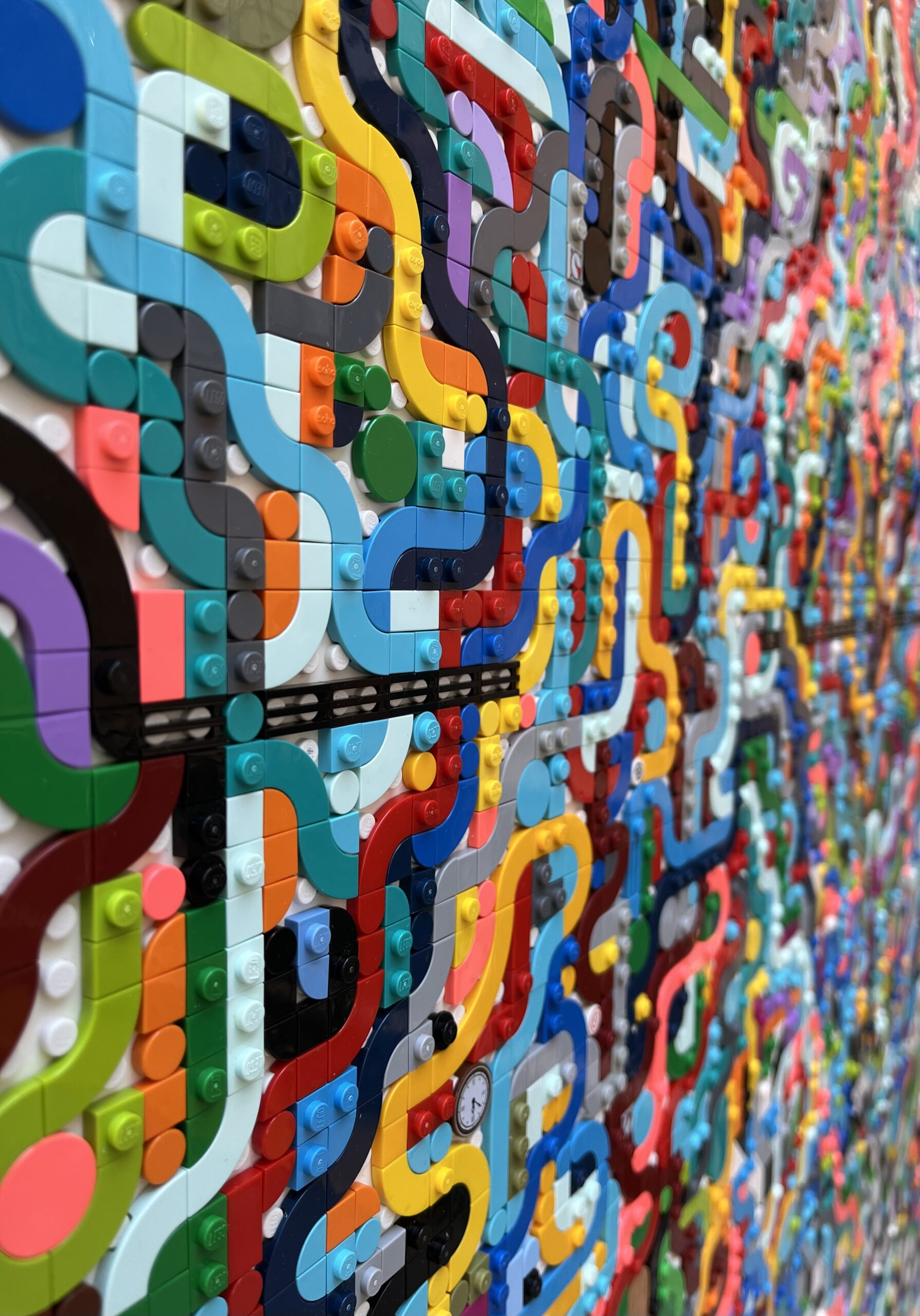 A sidelong view of a flat, painting-like artwork made of Lego bricks forming an abstract pattern, with a small clock face toward the lower section.