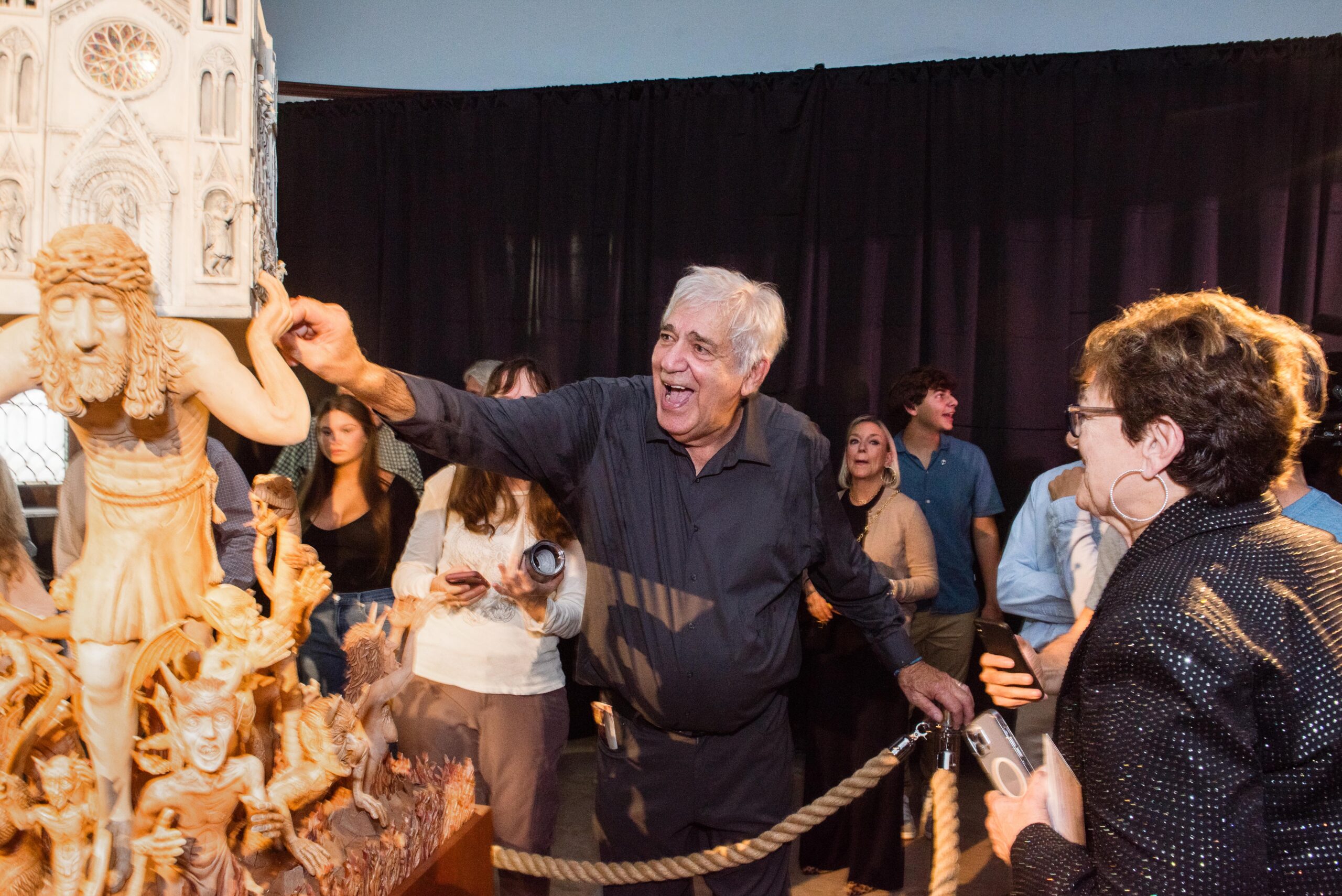 Amidst a group of onlookers, artist James Grashow reaches out to touch his sculpture, the Cathedral, depicting Christ carrying a church surrounded by fantastical creatures.