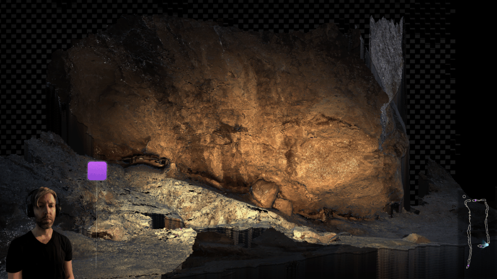 In a digital environment, a dramatic boulder rises in from a checkered void. In the bottom left hand corner, an avatar of Blake Marques Carrington stands, wearing a headset. On the bottom right of the image appears an unmarked map of a P-shaped route.