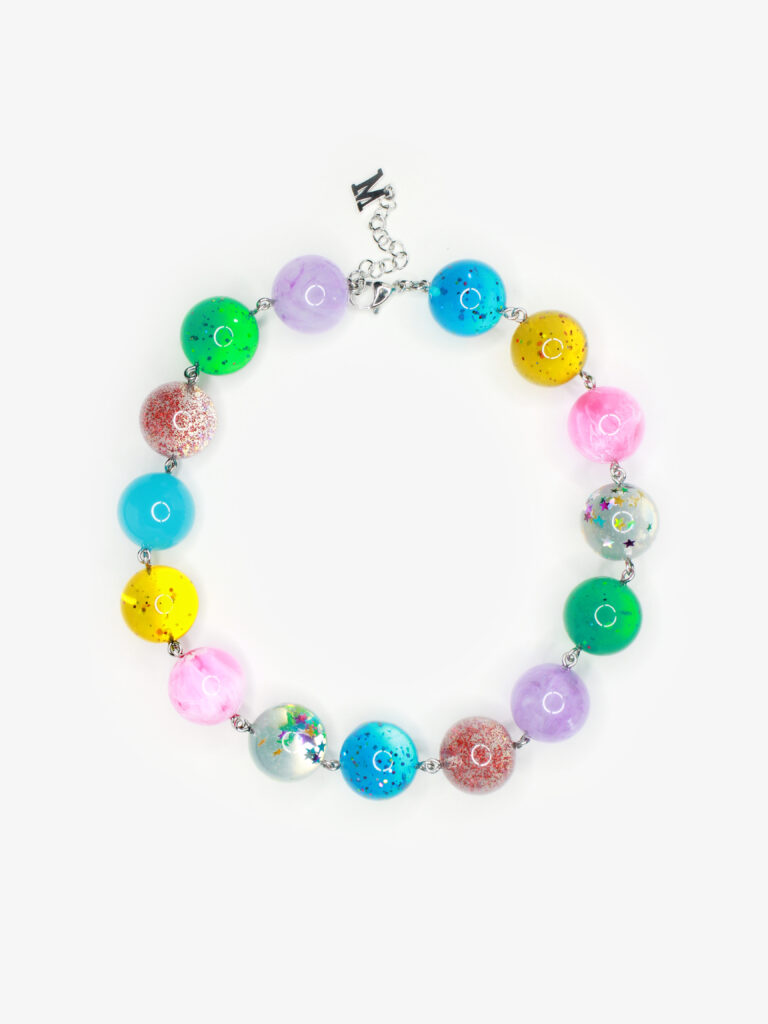 A necklace featuring bright multicolored semi-translucent beads embedded with glitter shaped like confetti and stars. Dangling from the necklace is a small silver charm in the shape of the letter "M." 