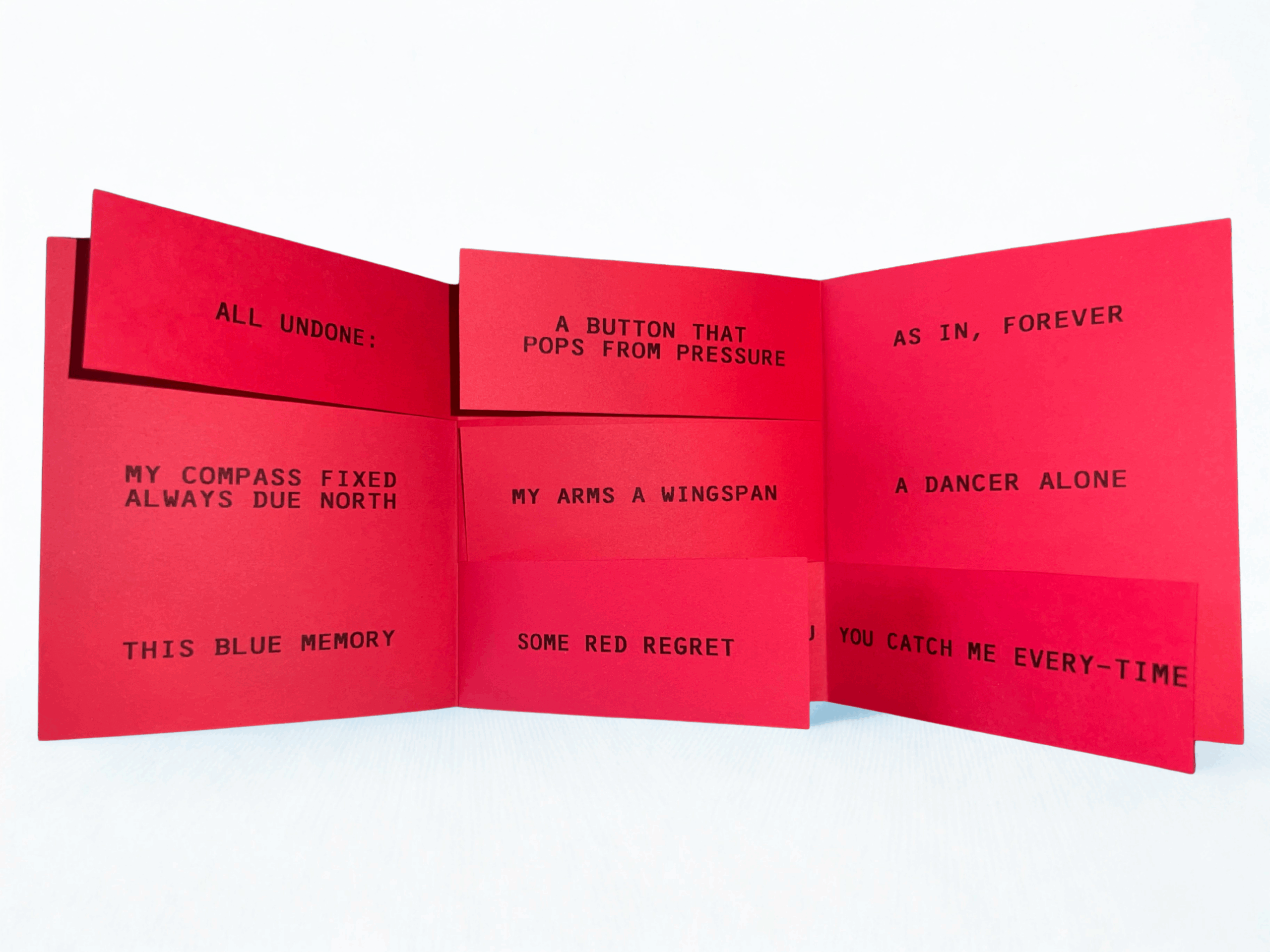 Expanded red accordion book displayed front-facing on a white background, featuring black uppercase text fragments such as “ALL UNDONE,” “MY ARMS A WINGSPAN,” “THIS BLUE MEMORY,” “SOME RED REGRET,” and “A DANCER ALONE,” arranged across interconnected folded panels.
