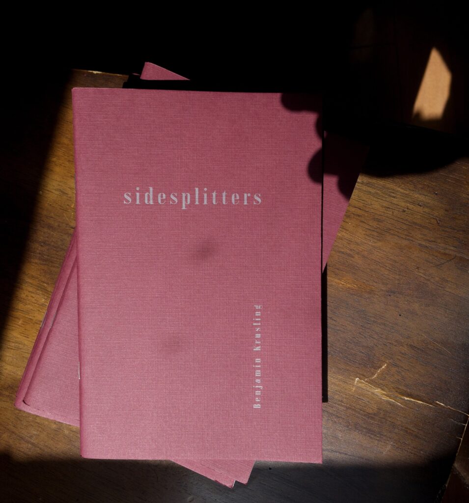 Printed copies of “Sidesplitters” are stacked on a wood-paneled background.