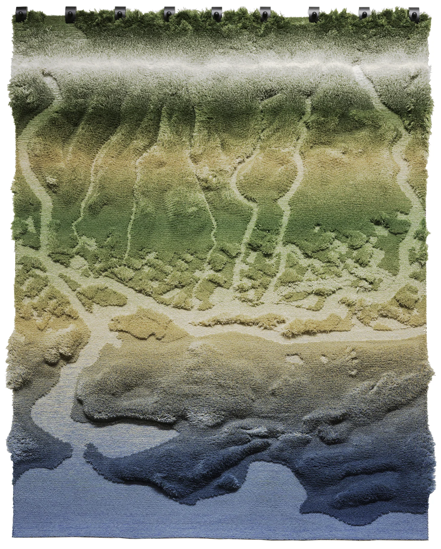 Large textile wall hanging with a sculptural, tufted surface forming an abstract landscape. The rug transitions vertically from deep blue at the bottom to sandy beige, then olive and dark green at the top, resembling waterways, erosion patterns, and vegetation seen from an aerial perspective. The piece is mounted with visible hardware along the top edge against a neutral background.